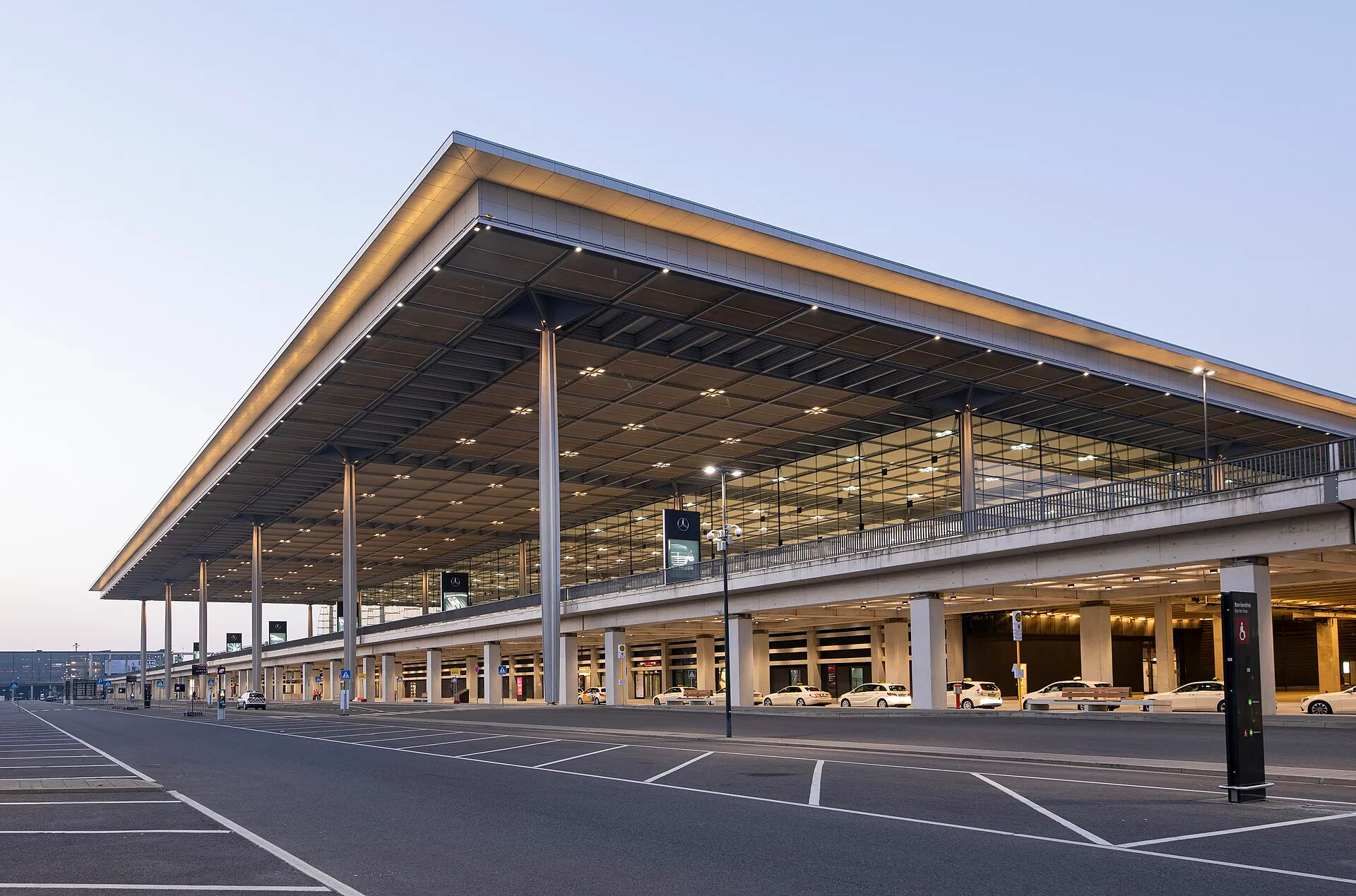 Vue extérieure du terminal 1 de l'aéroport de Berlin-Brandebourg (BER) au crépuscule, son long toit en porte-à-faux surplombant les voies d'accès