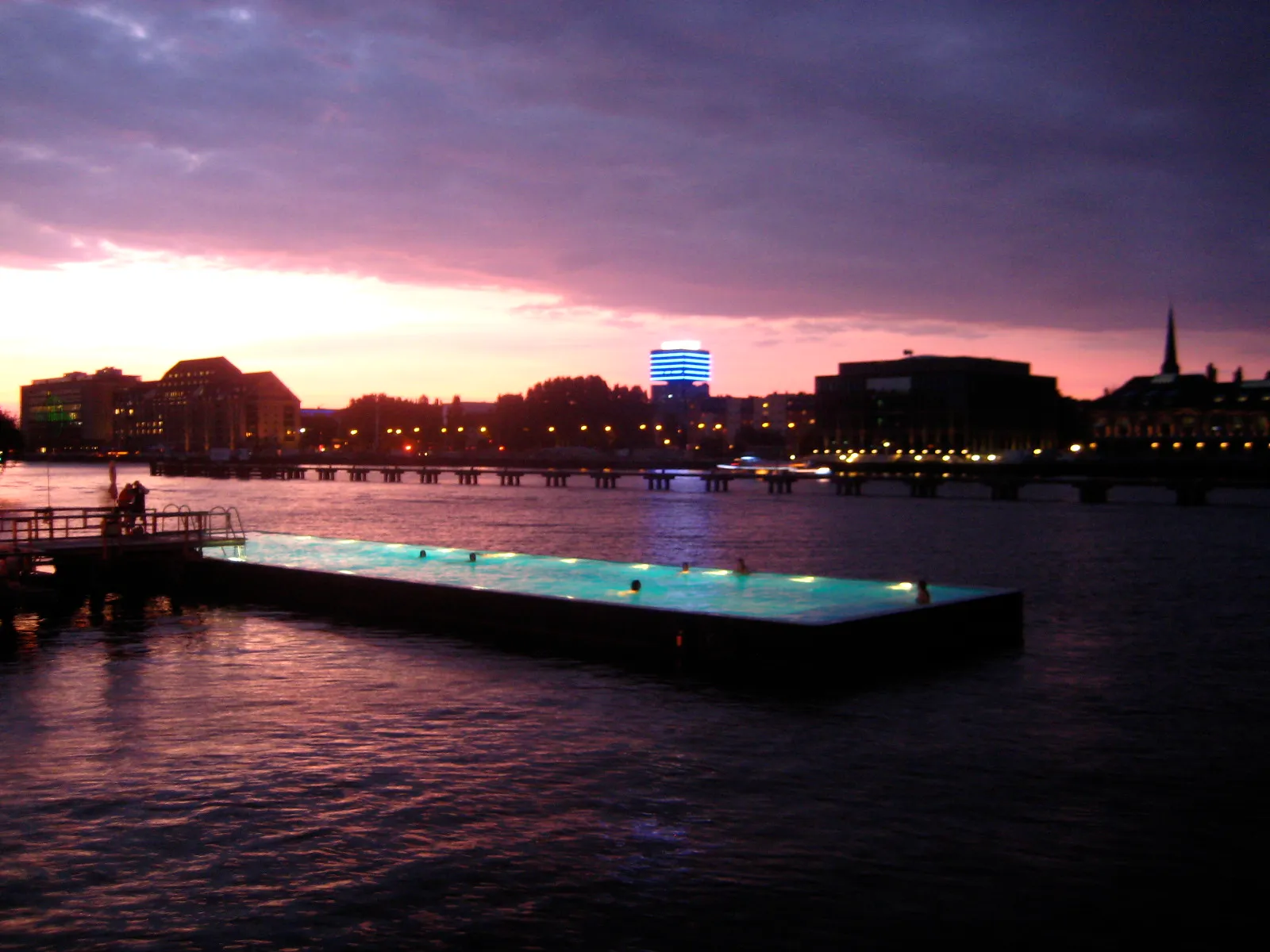 Le Badeschiff au coucher du soleil, piscine flottante illuminée sur la Spree avec des nageurs