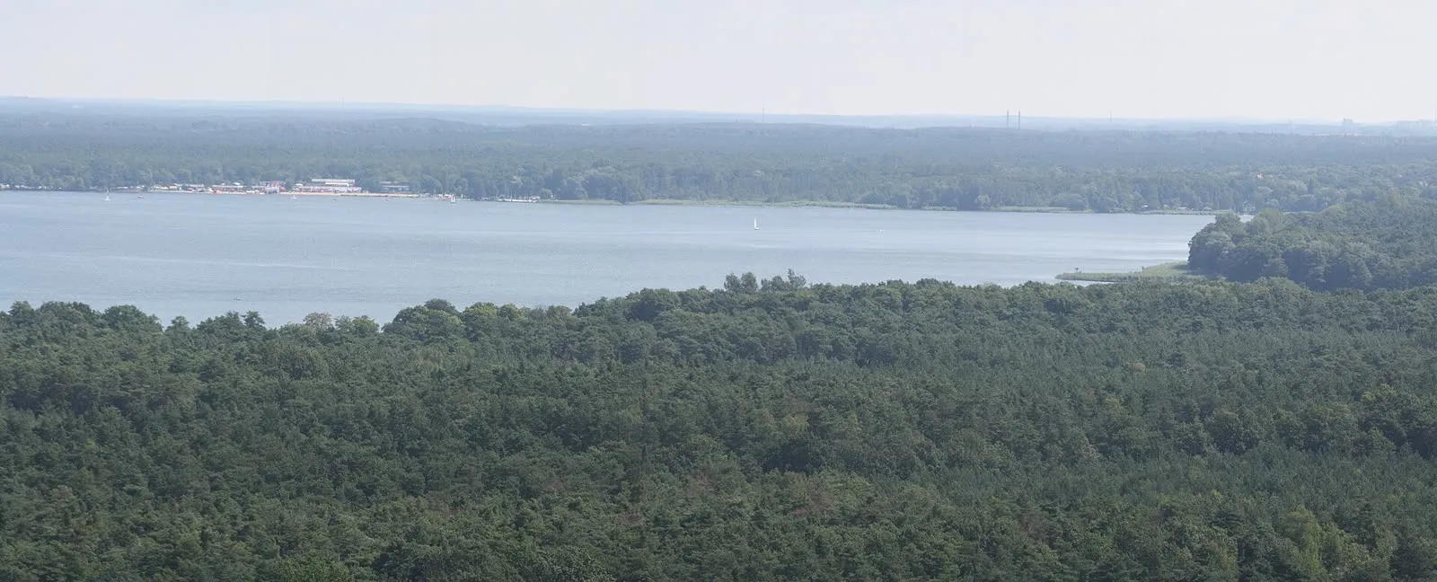 Vue plongeante sur le Müggelsee depuis les hauteurs boisées, avec un voilier et les rives bâties au loin