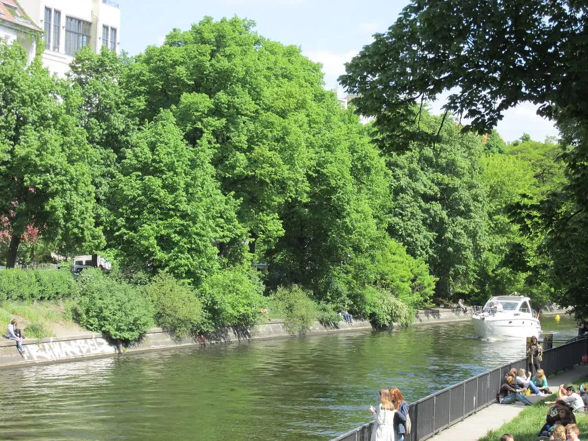 Le Landwehrkanal au printemps, promeneurs sur la berge aménagée, arbres feuillus et bateau sur l'eau
