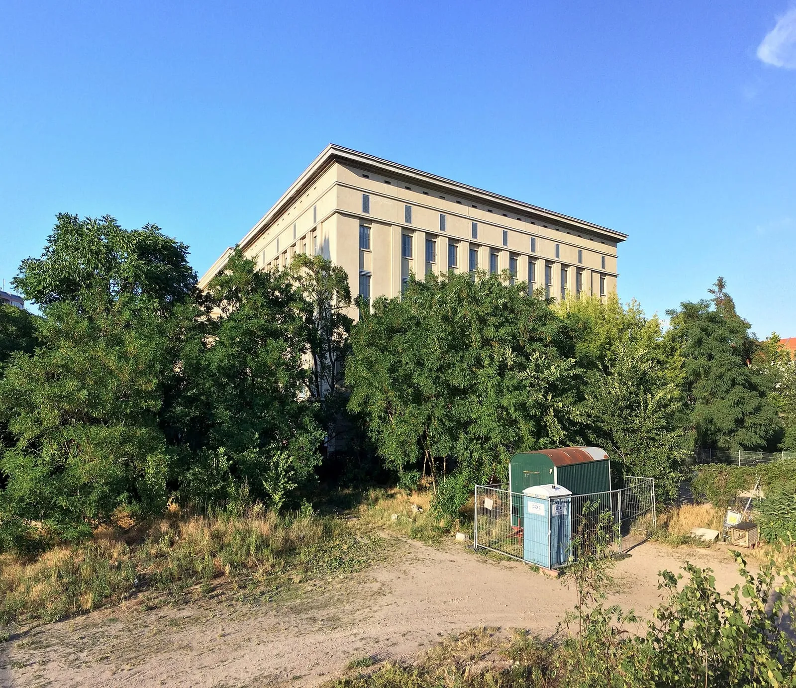Le bâtiment beige de l'ancienne centrale de chaleur et d'électricité de Friedrichshain, vu de jour derrière des arbres