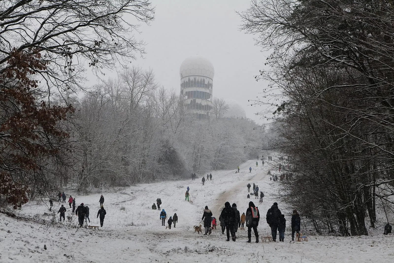 Des familles descendent la pente enneigée du Teufelsberg à la luge, la coupole radar de l'ancienne station d'écoute dans la brume au sommet