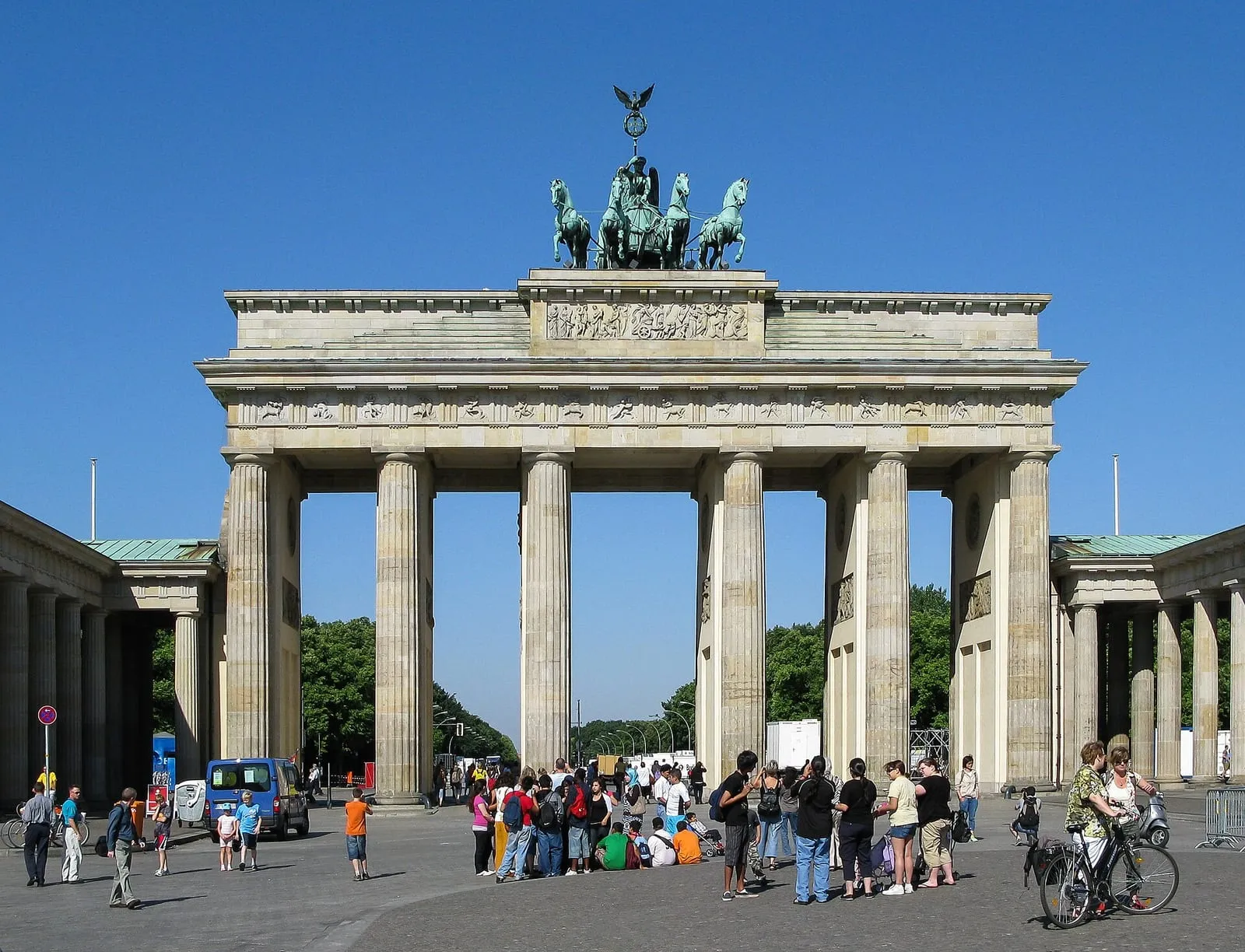 Touristes et cyclistes rassemblés devant la porte de Brandebourg à Berlin, sous la quadrige, par une journée ensoleillée