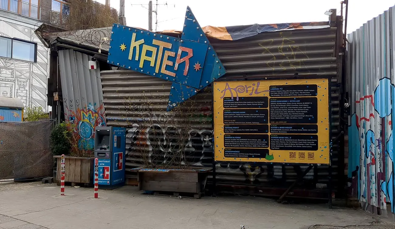 L'enseigne bleue en forme de flèche du club Kater au Holzmarkt, sur des parois de conteneurs graffitées