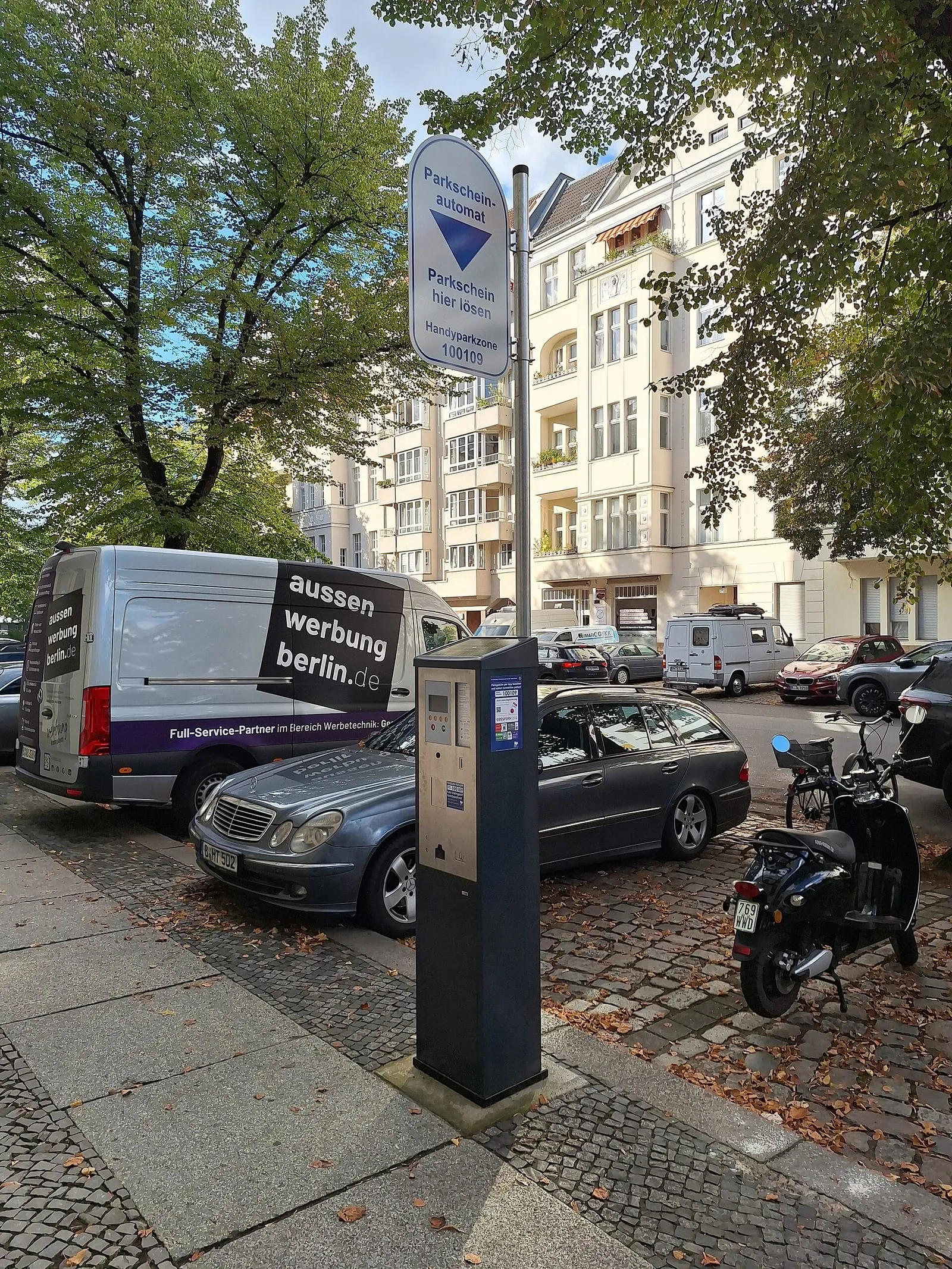 Horodateur de stationnement sur un trottoir berlinois, devant des voitures garées le long d'une rue pavée