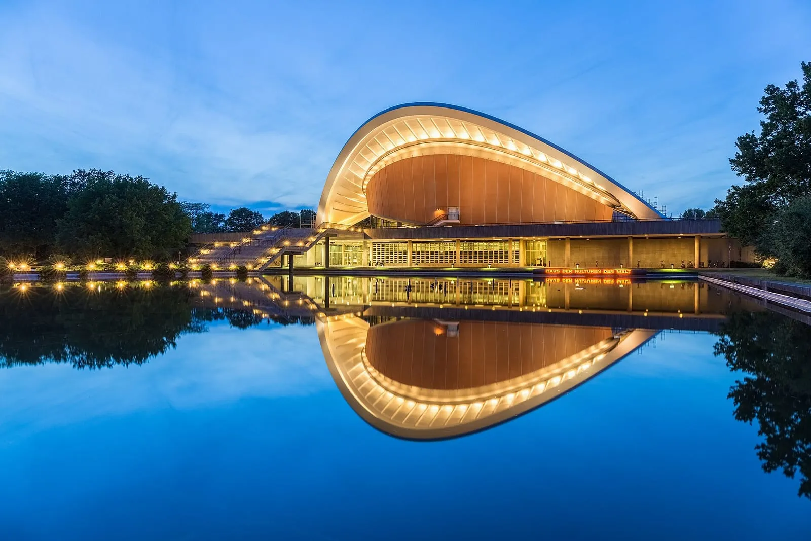 Le Haus der Kulturen der Welt à l'heure bleue, sa toiture courbe éclairée se reflétant dans la Spree