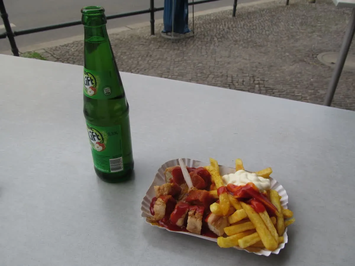 Une currywurst coupée en rondelles servie avec des frites et de la mayonnaise dans une barquette en carton