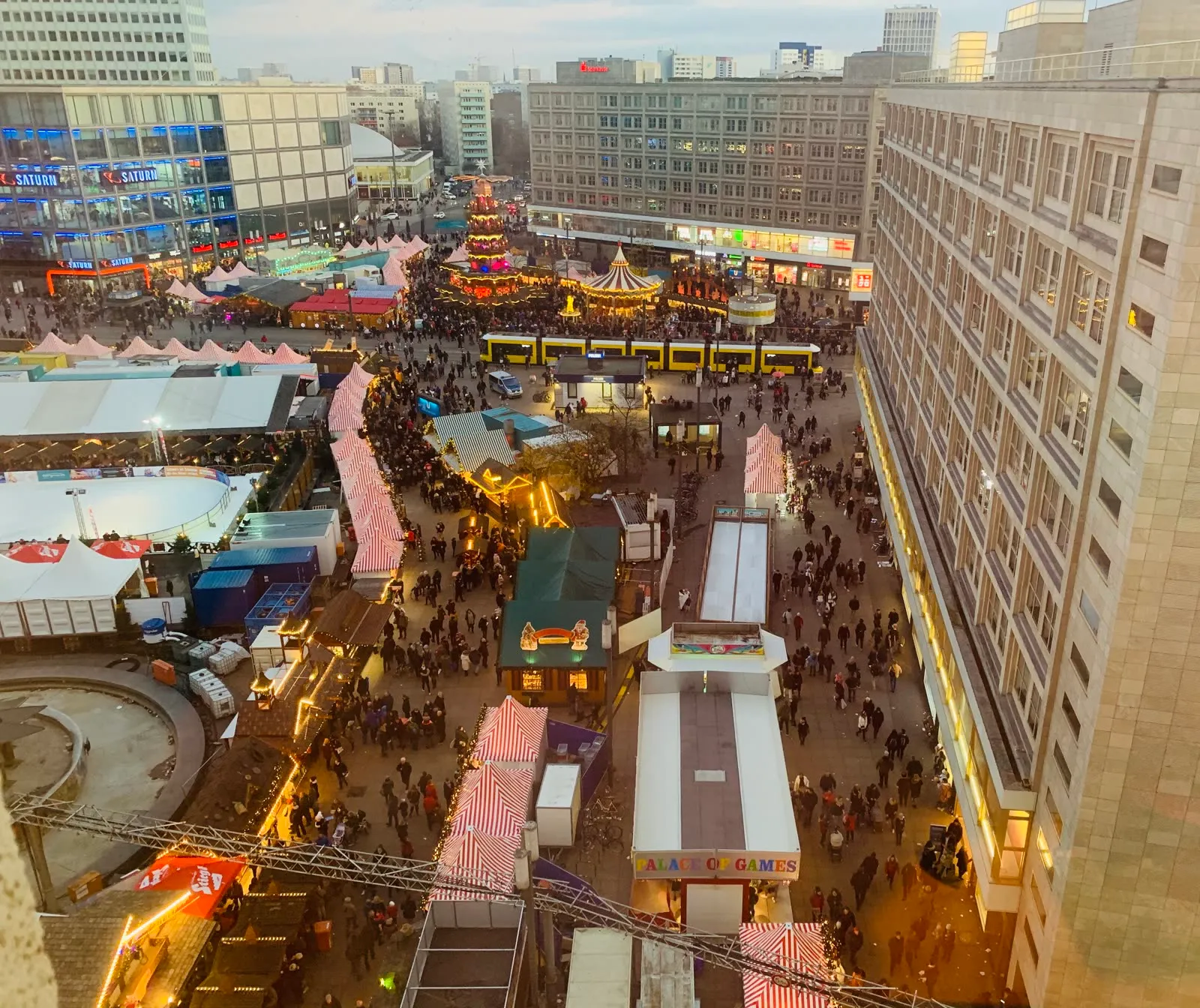 Vue plongeante sur le marché de Noël de l'Alexanderplatz au crépuscule, entre les chalets, le grand sapin, la patinoire et les voies du tramway