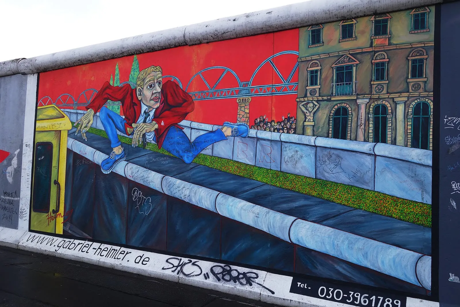La fresque du sauteur de mur de Gabriel Heimler, un homme en blouson rouge qui enjambe le béton, l'Oberbaumbrücke peinte en arrière-plan