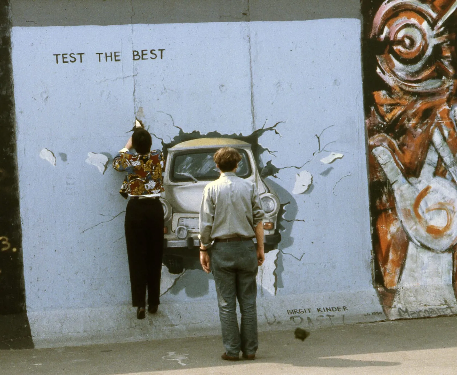 Deux visiteurs devant la Trabant qui traverse le mur, fresque « Test the Best » de Birgit Kinder