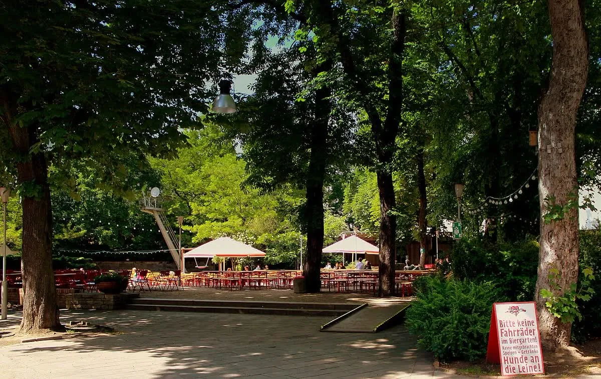Tables et bancs en bois sous les arbres d'un biergarten berlinois, avec parasols et guirlandes lumineuses