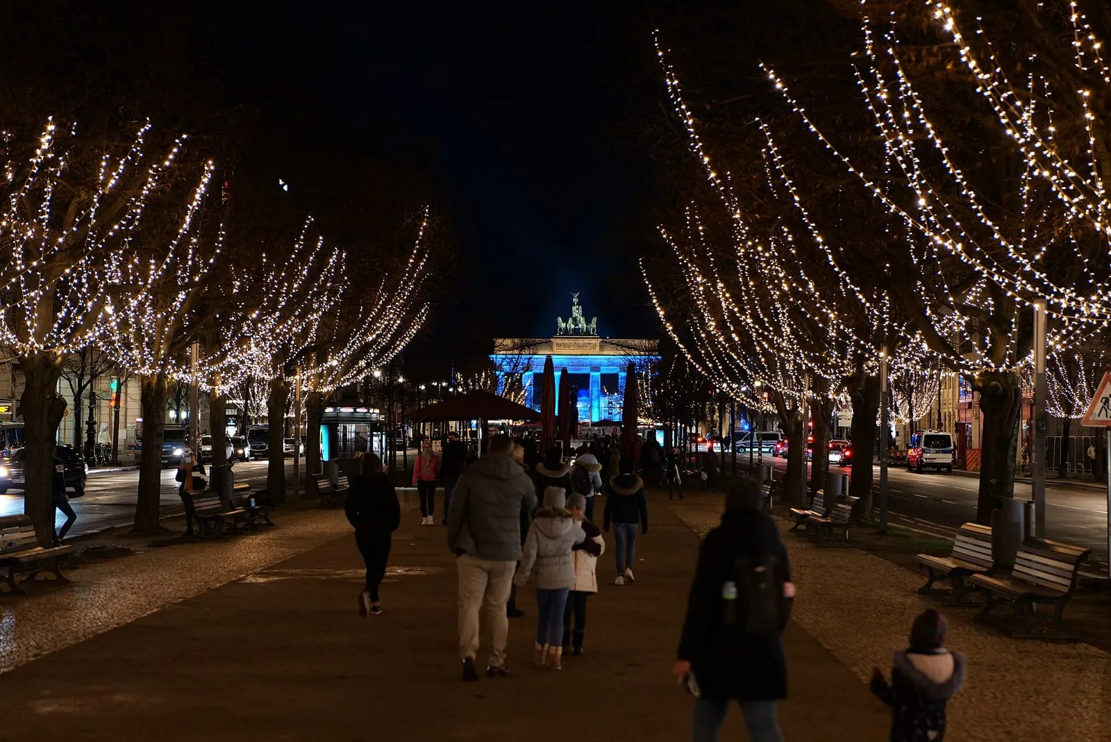 La porte de Brandebourg éclairée en bleu la nuit, au bout d'une allée d'arbres garnis de guirlandes lumineuses