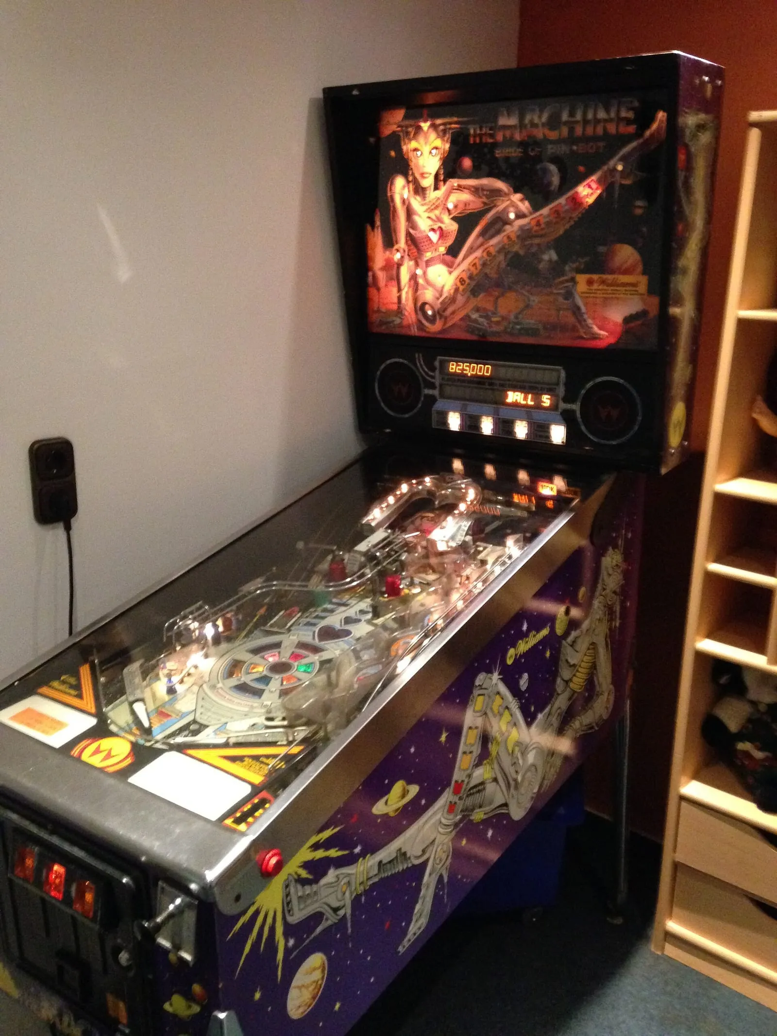 Un flipper rétro au plateau illuminé, prêt à jouer, dans une petite salle de jeux