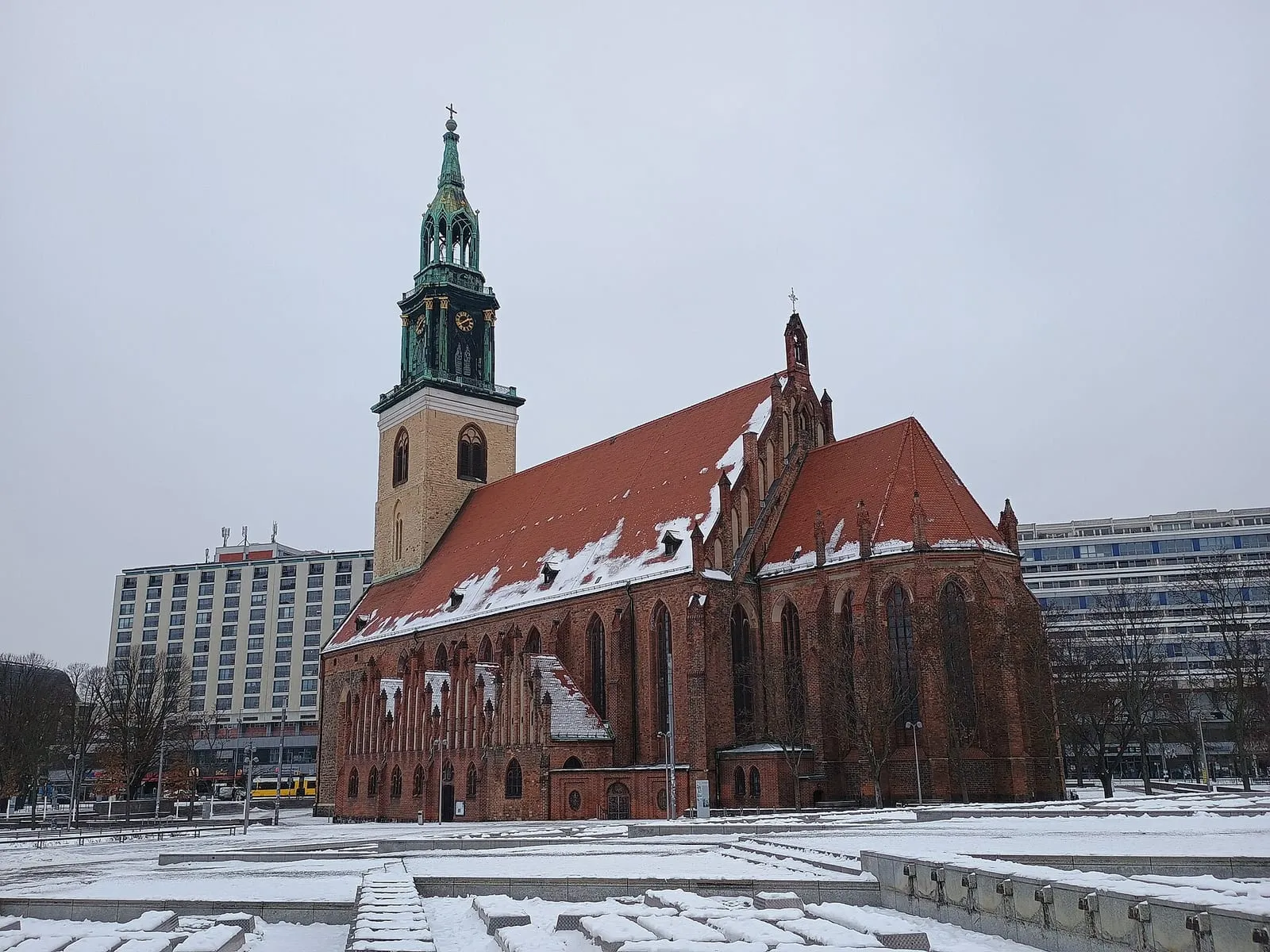 La Marienkirche et sa place enneigée près d'Alexanderplatz, un tramway et des façades d'immeubles sous un ciel d'hiver gris à Berlin