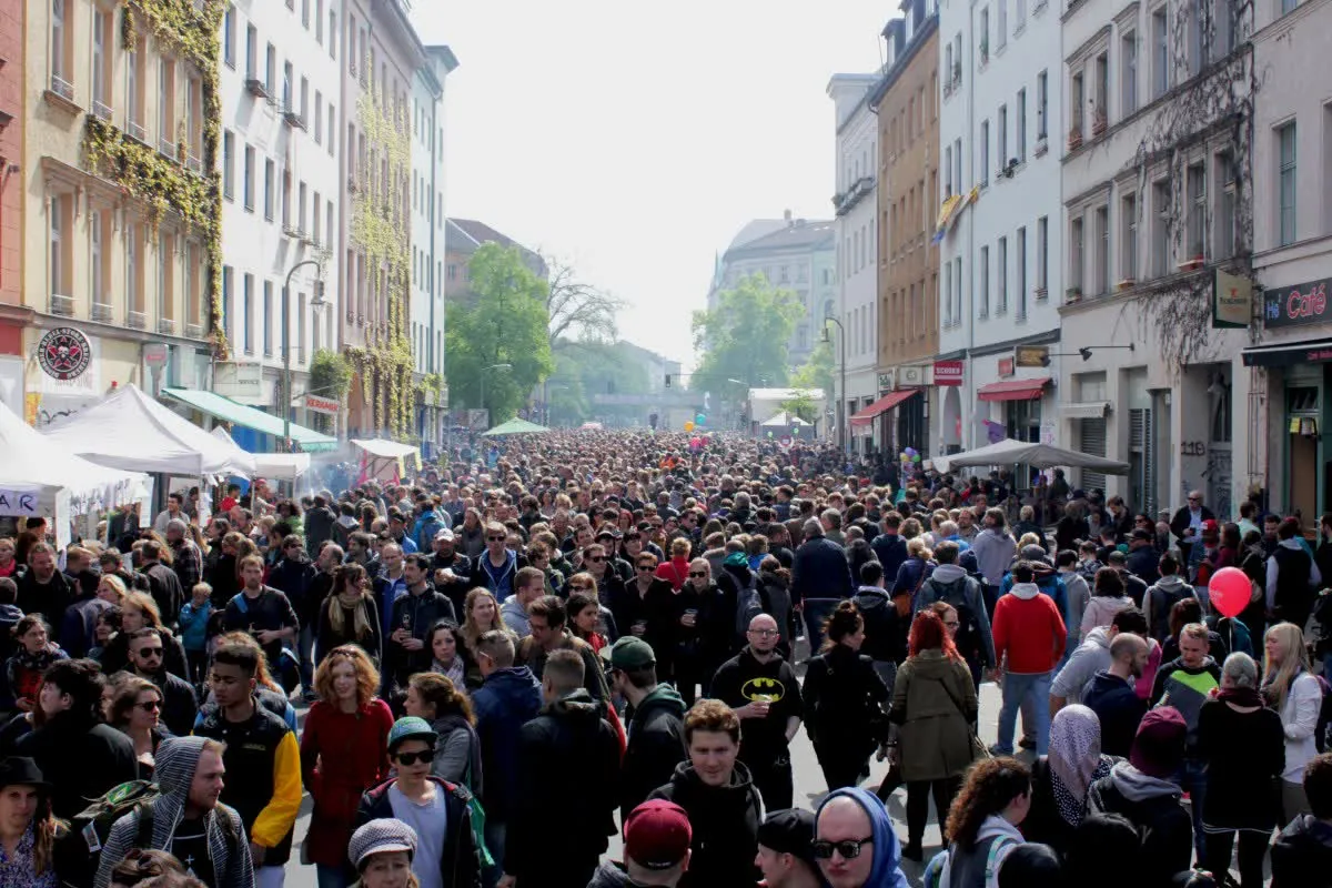 Foule dense dans une rue de Kreuzberg pendant le Myfest du 1er mai, entre barnums blancs, stands et façades d'immeubles anciens