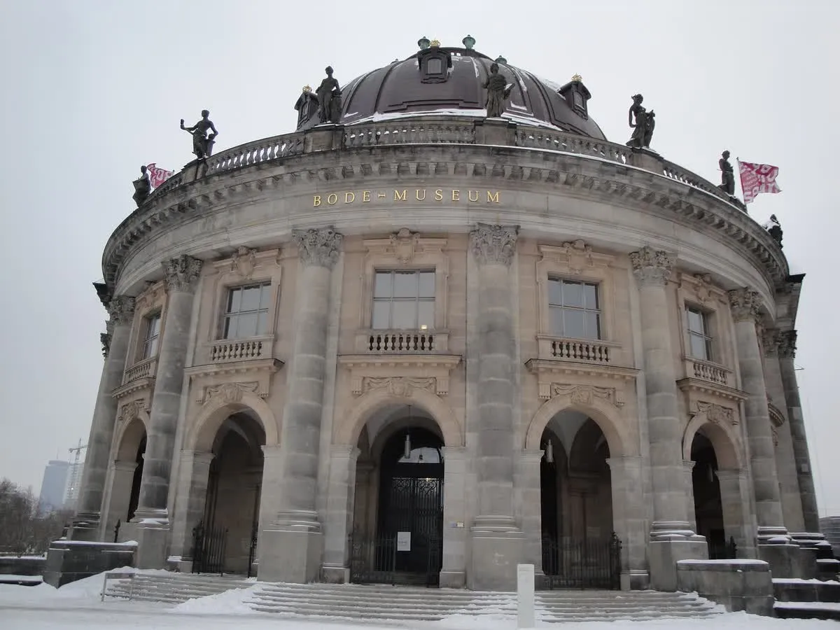 La façade arrondie du Bode Museum sous la neige, escaliers et coupole blanchis, sous un ciel d'hiver uniformément gris