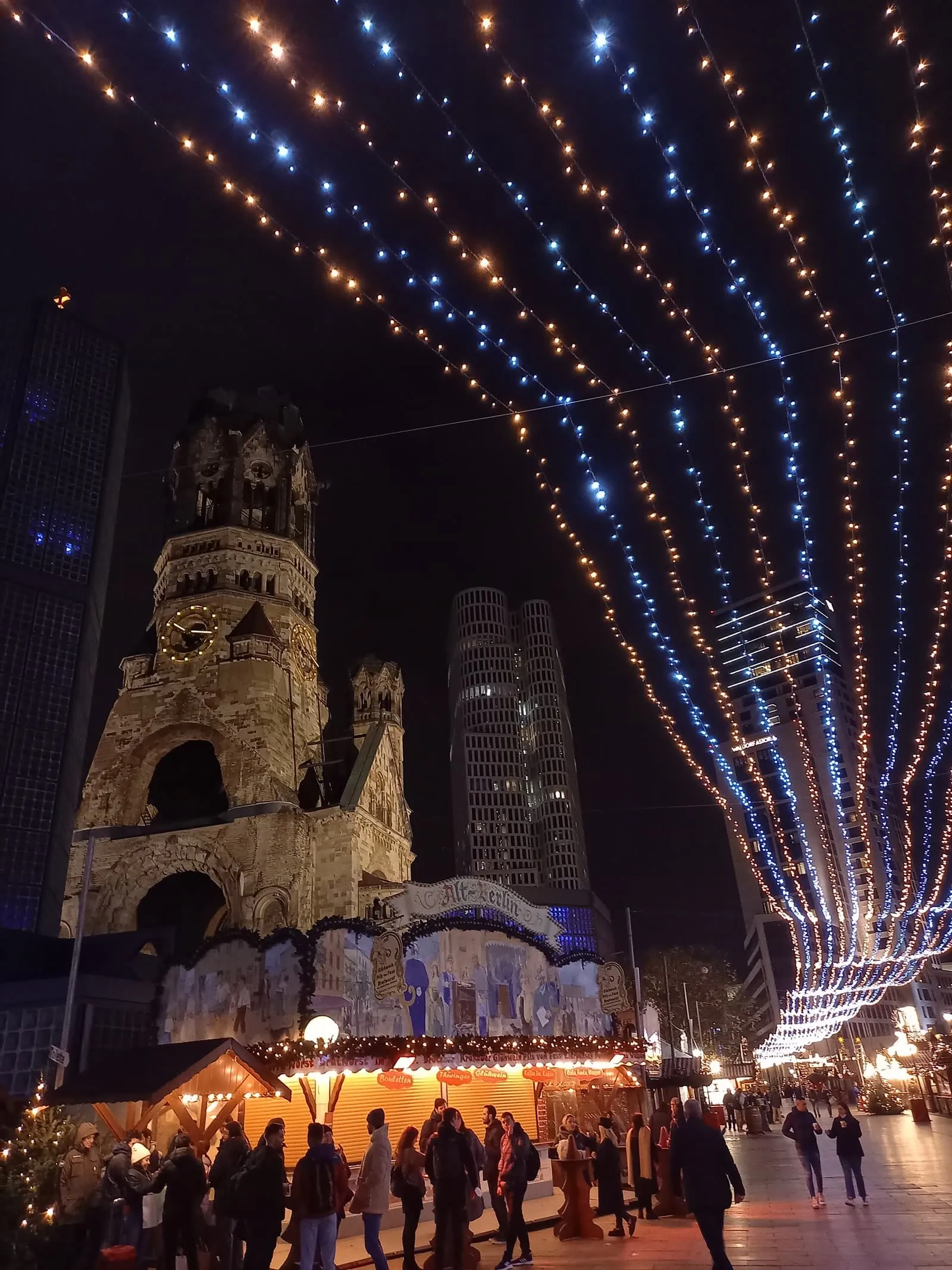 Le marché de Noël de la Breitscheidplatz au pied de la Gedächtniskirche, sous un dais de guirlandes bleues et dorées, avec le stand Alt-Berlin et sa tour en ruine éclairée