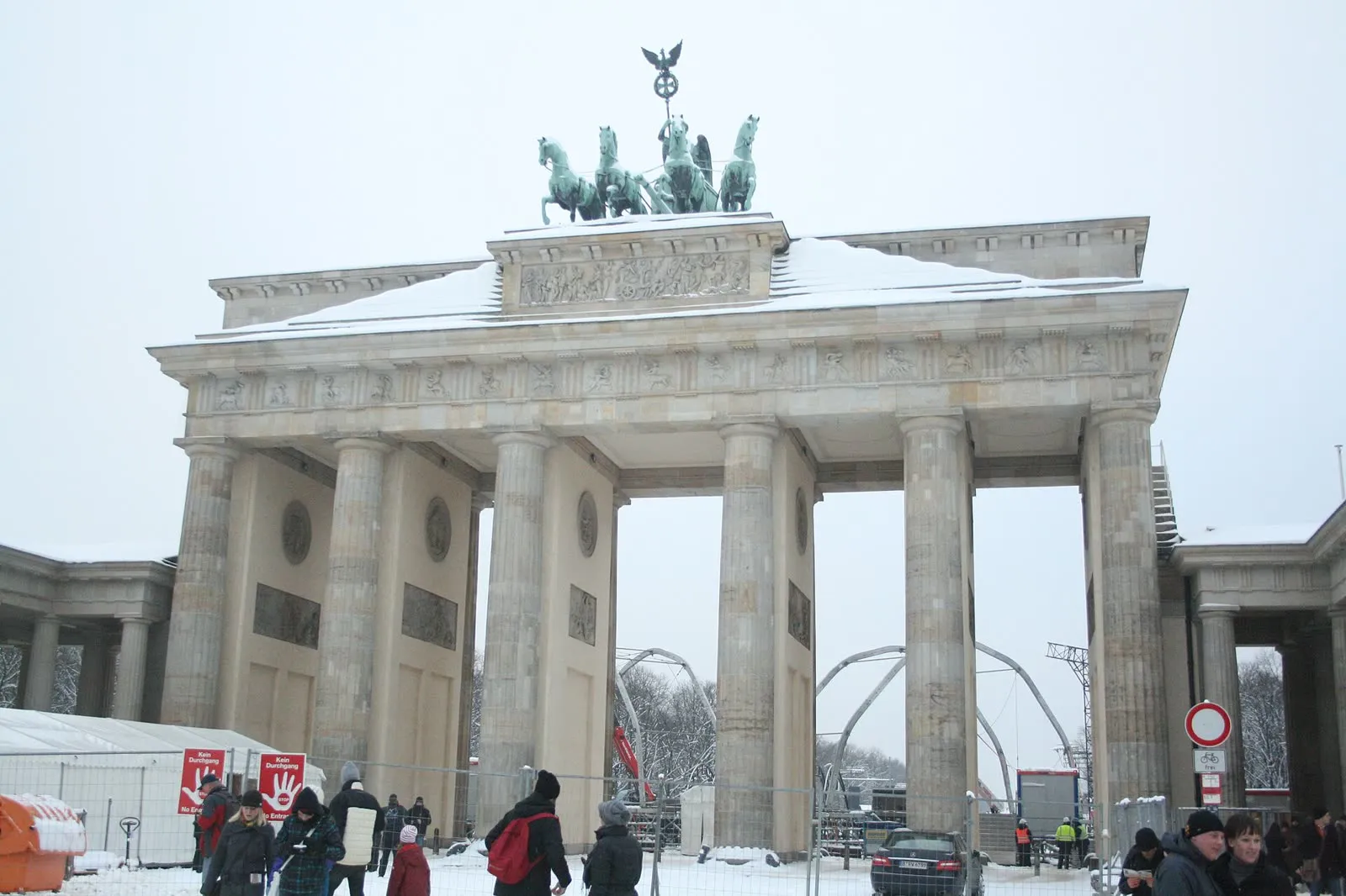 La porte de Brandebourg un matin d'hiver enneigé, la quadrige et les colonnes sous un ciel blanc, des piétons emmitouflés traversant la Pariser Platz