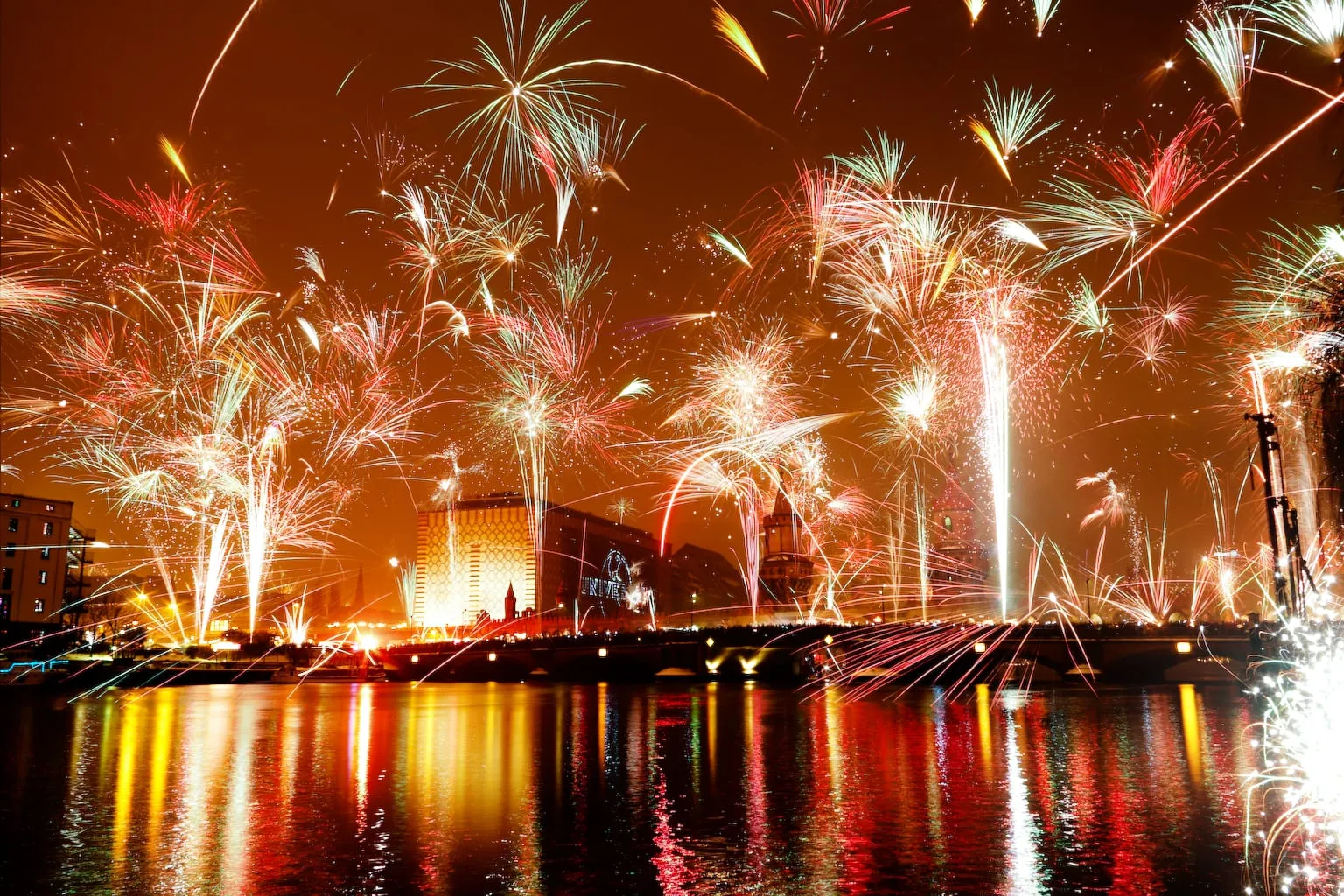 Feux d'artifice du Nouvel An au-dessus de la Spree à Berlin, reflets dans l'eau et foule massée sur un pont