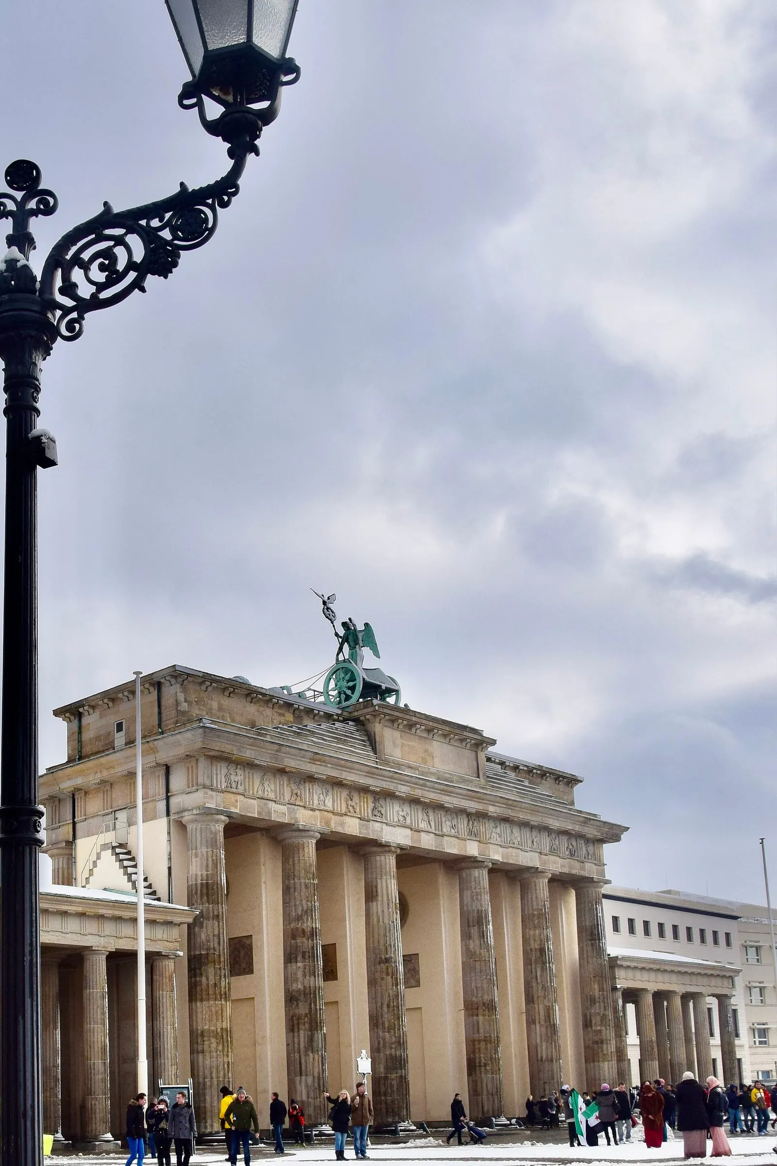 La porte de Brandebourg à Berlin un jour d'hiver, sous un ciel gris, avec la place enneigée et des passants devant le monument