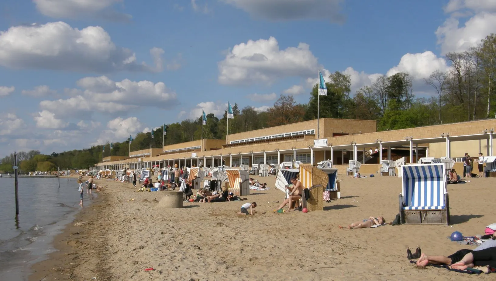 La plage du Strandbad Wannsee : sable, chaises longues rayées et long bâtiment au bord du lac, sous un ciel d'été
