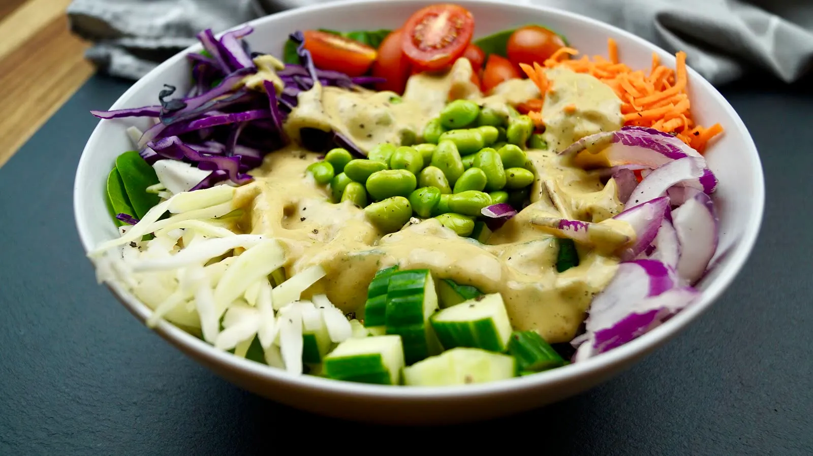Un bowl végétal garni de jeunes pousses, de tomates cerises, de chou rouge, de concombre et d'edamame, nappé d'une sauce crémeuse