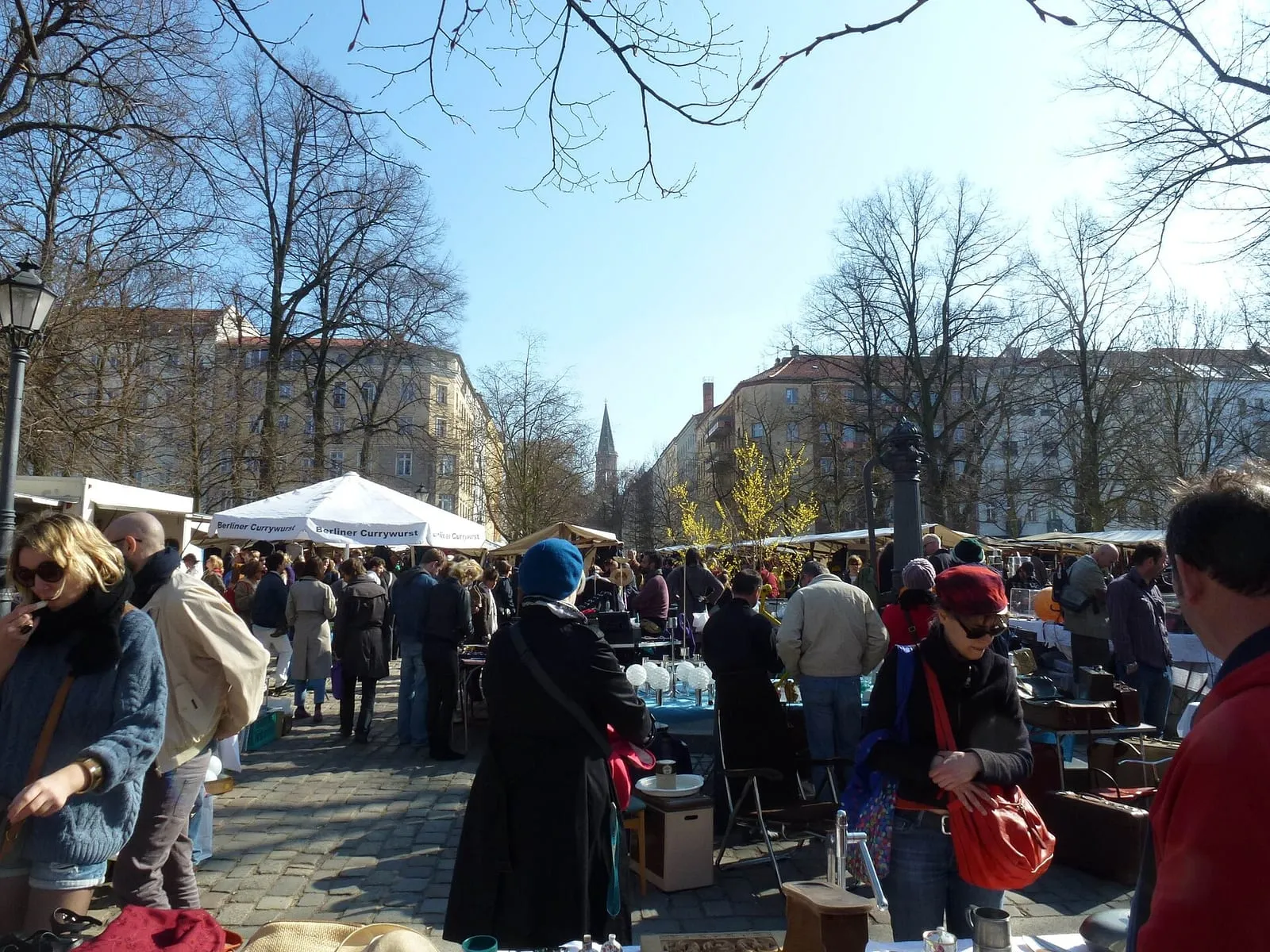 Étals de brocante sur le pavé de l'Arkonaplatz, à Berlin-Mitte, avec un stand de currywurst en arrière-plan