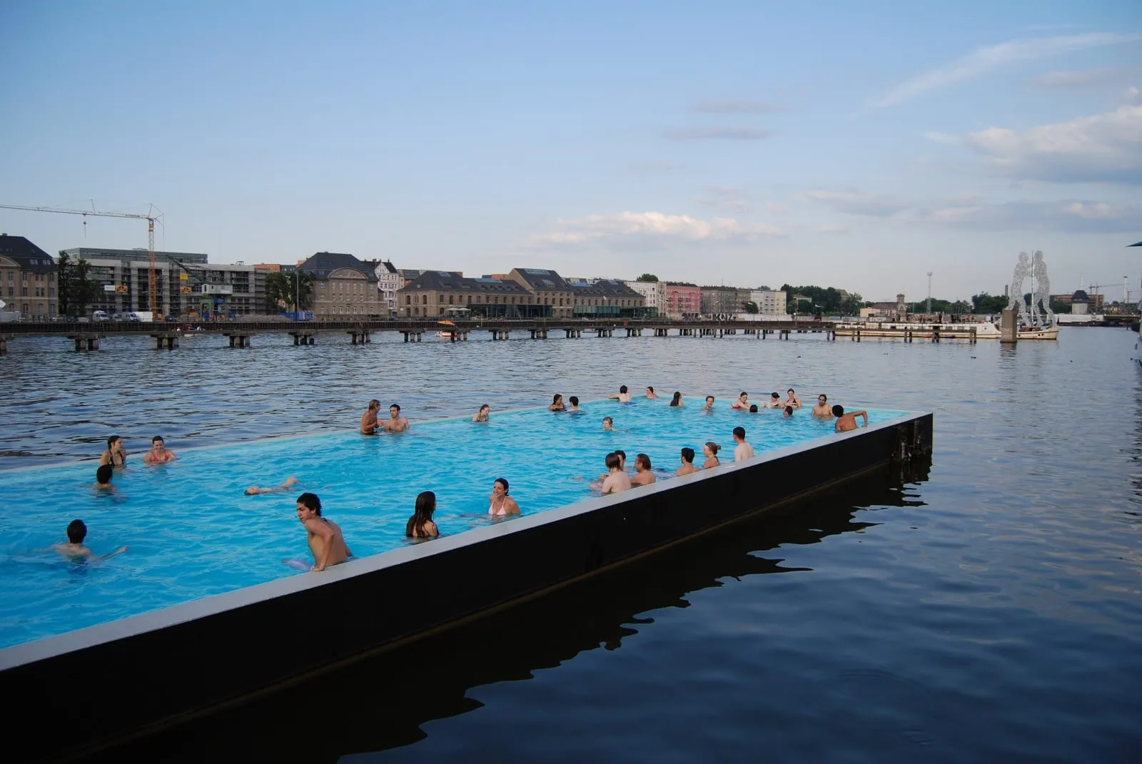 Le Badeschiff, piscine flottante sur la Spree, avec des baigneurs dans le bassin et la sculpture Molecule Man à proximité