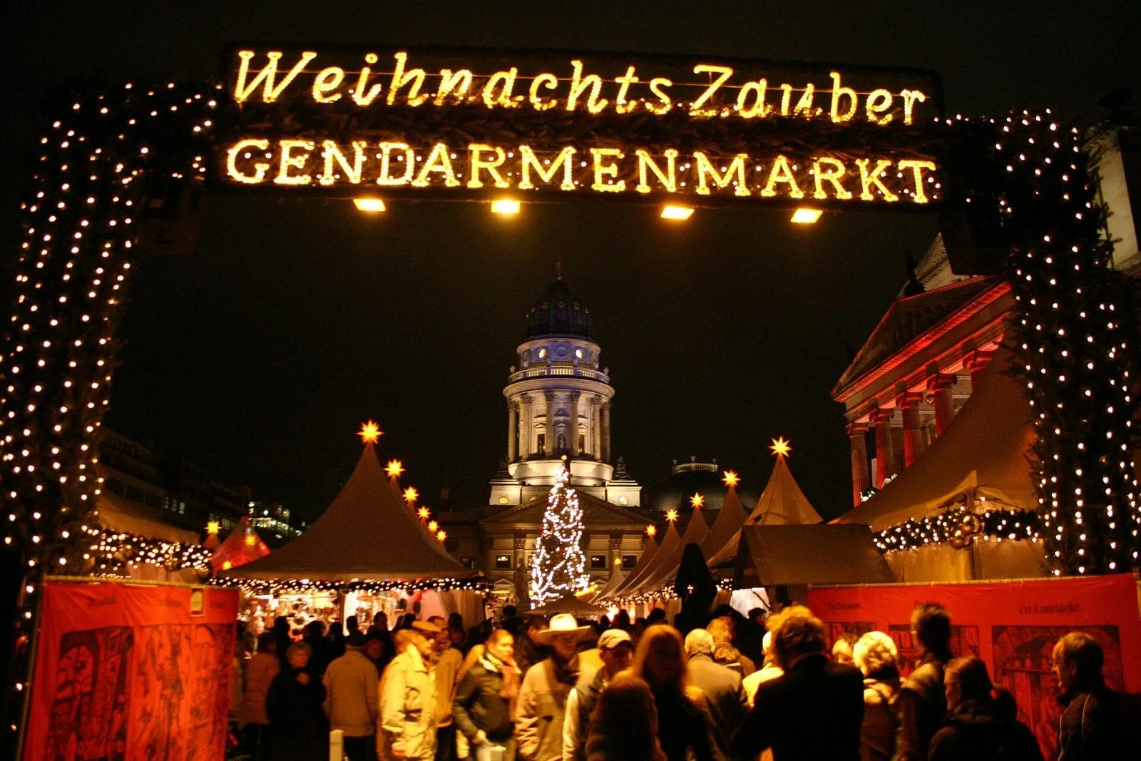 Le marché de Noël du Gendarmenmarkt la nuit, sous l'arche lumineuse du WeihnachtsZauber, les tentes et le grand sapin éclairés devant la cathédrale française