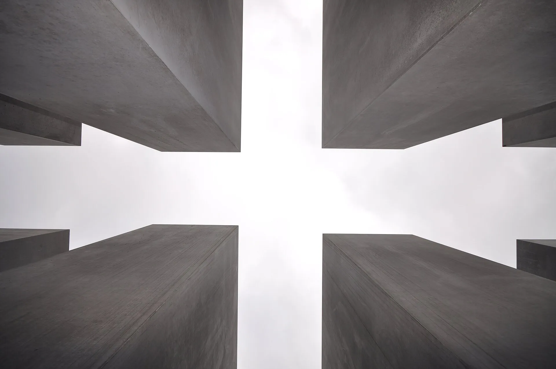 Quatre stèles de béton vues d'en bas, encadrant un carré de ciel blanc au-dessus du champ du mémorial
