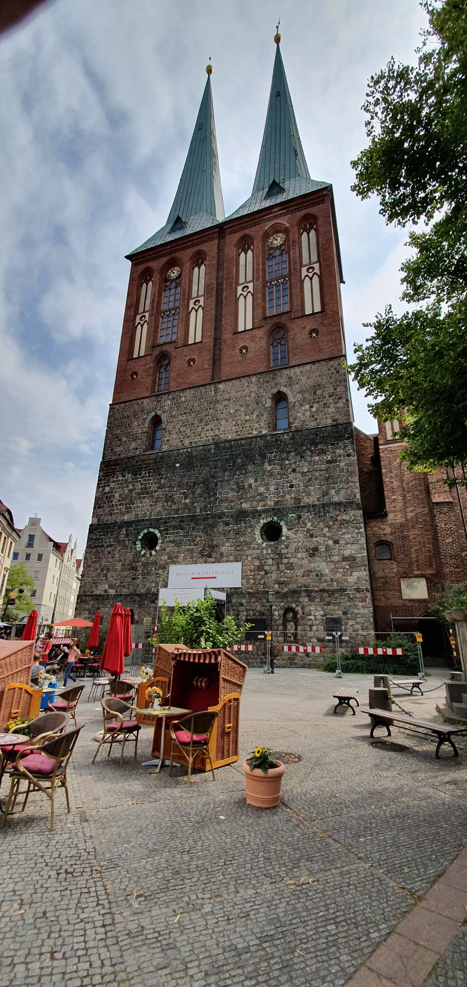 Les deux clochers de la Nikolaikirche vus depuis le Nikolaikirchplatz, avec des tables de café au premier plan
