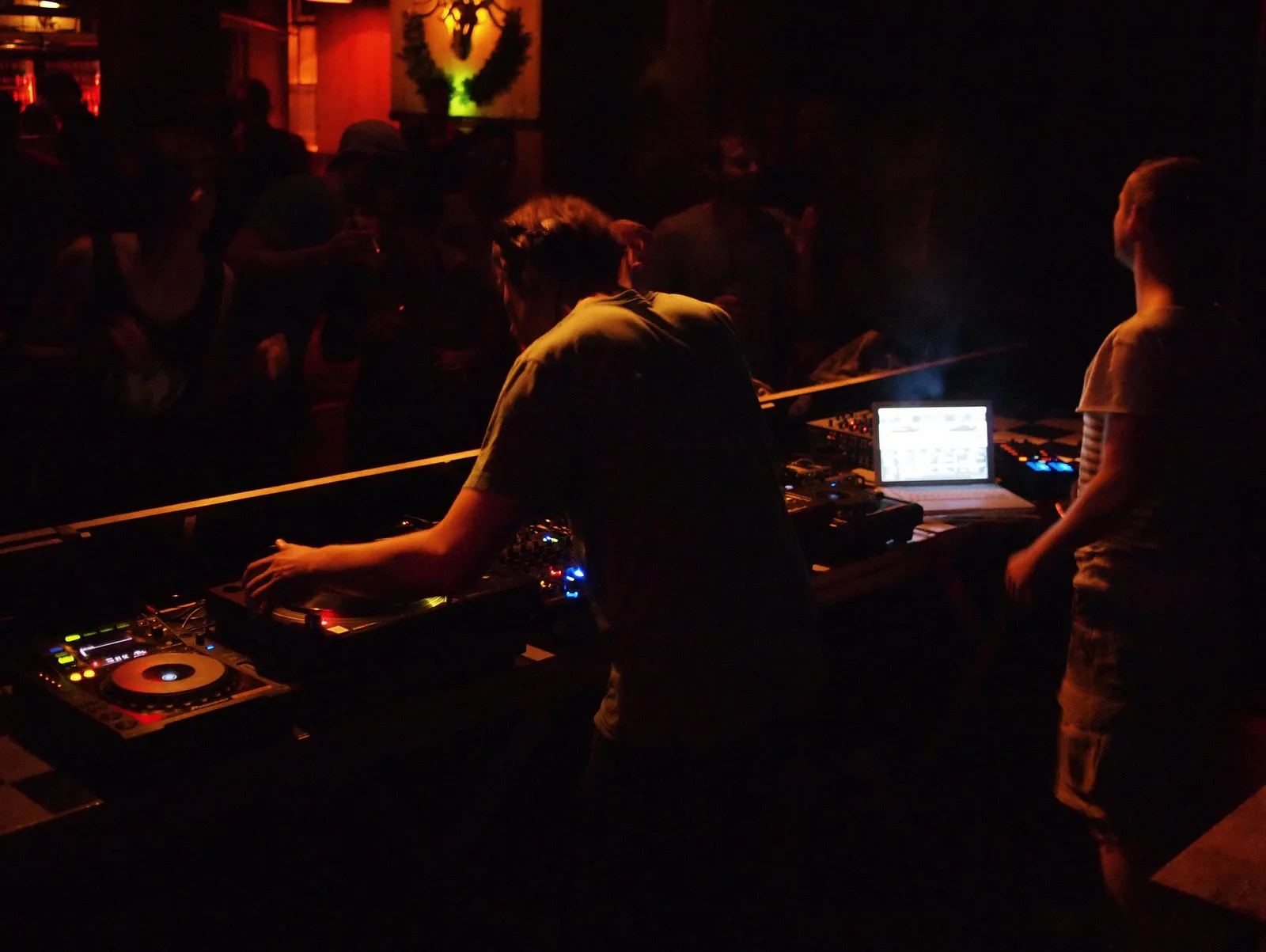Un DJ vu de dos mixe dans la pénombre rouge d'un club berlinois, devant une foule en silhouette