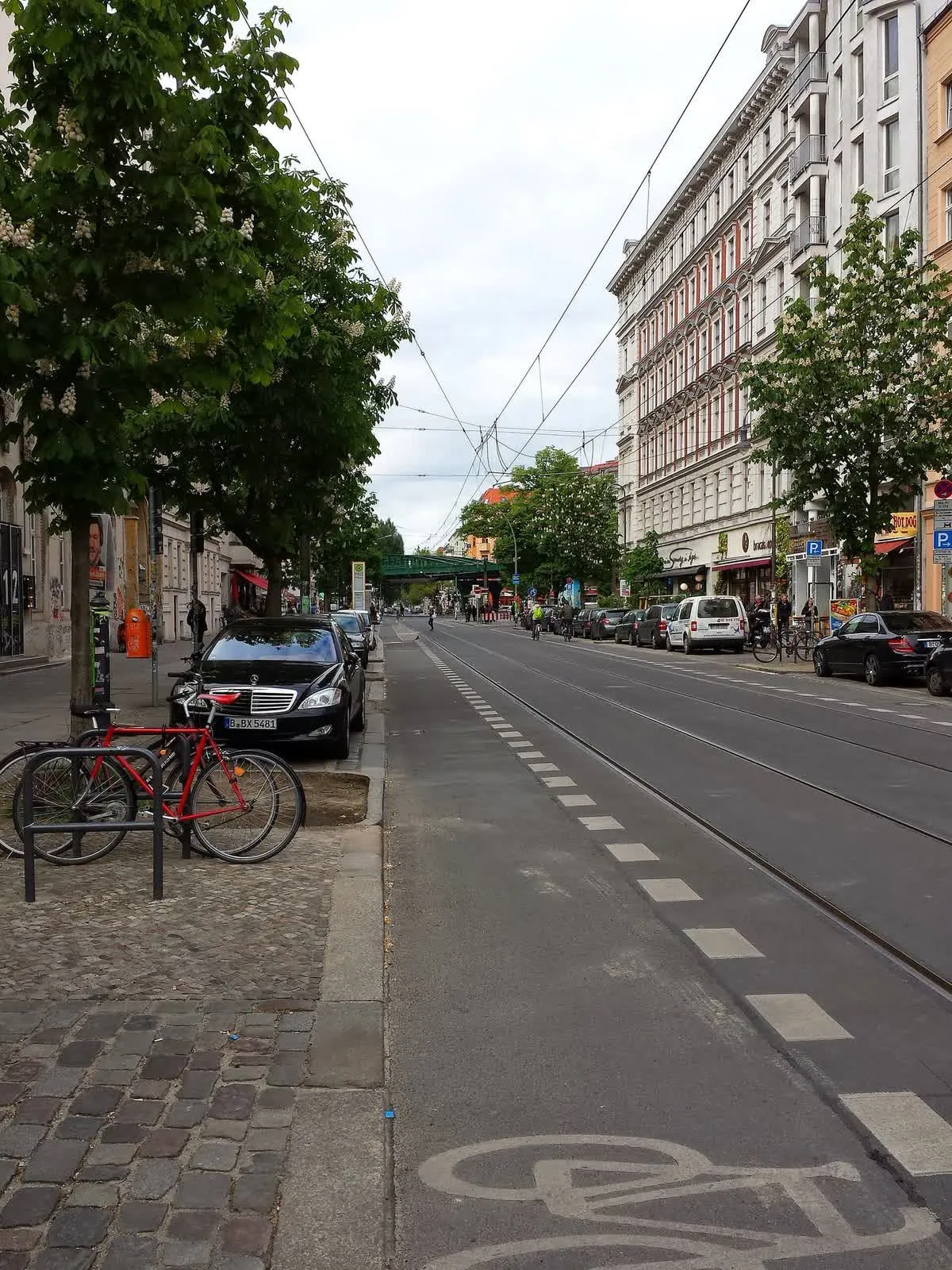 La Kastanienallee à Prenzlauer Berg, ses rails de tramway, ses immeubles anciens et ses arbres, avec un cycliste au loin