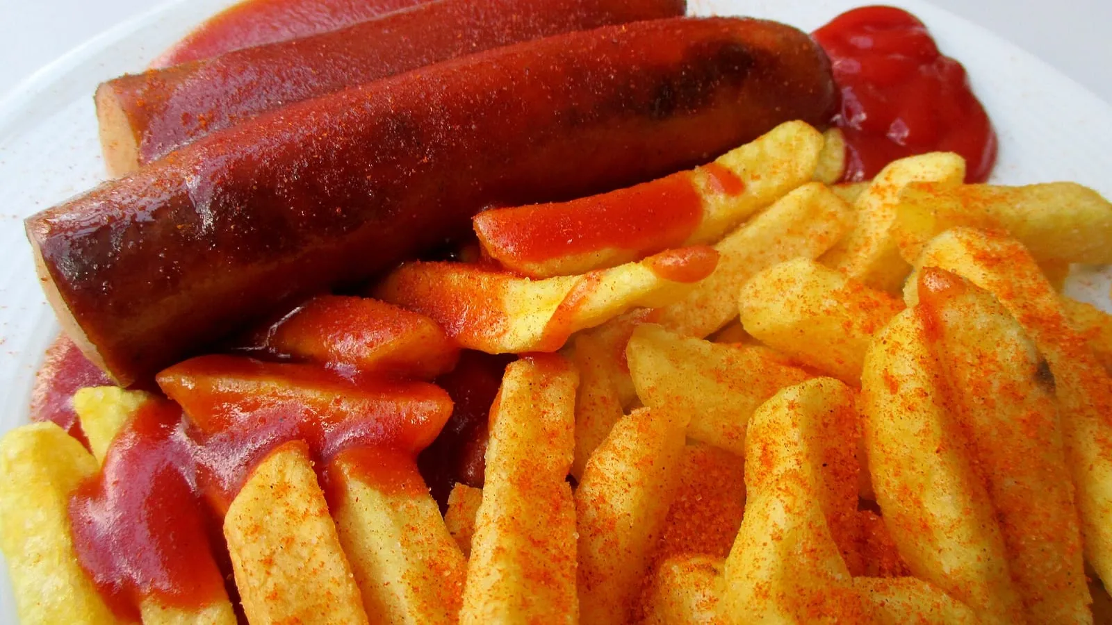Une currywurst coupée en rondelles, nappée de sauce tomate au curry, servie avec des frites