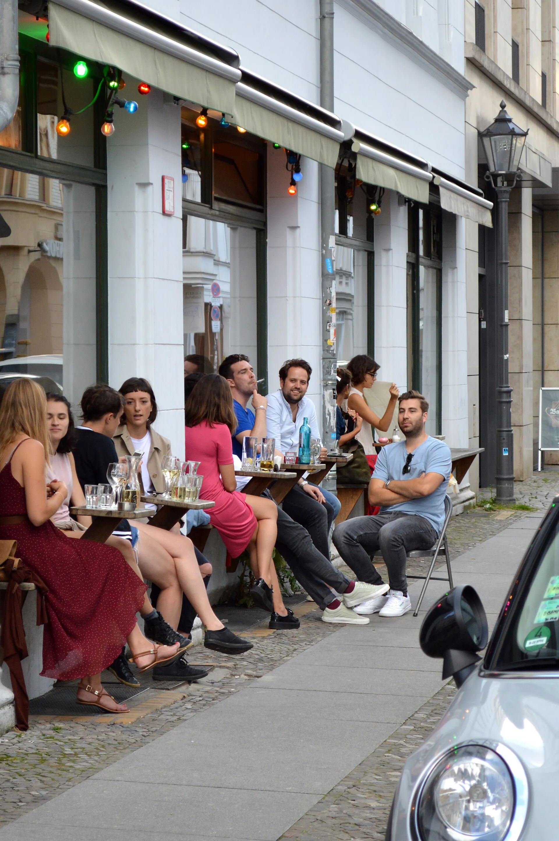 Terrasse de café berlinois : clients attablés devant la façade, guirlandes lumineuses sous l'auvent