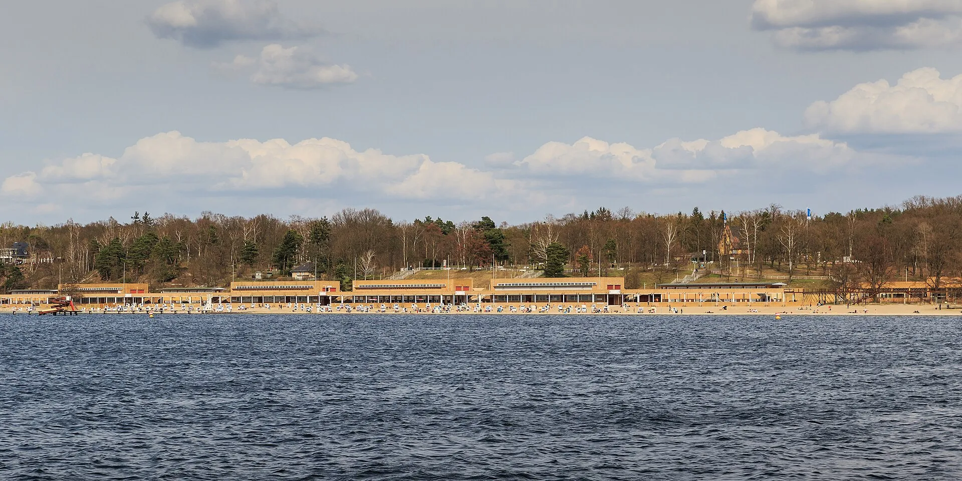 Le Strandbad Wannsee vu depuis le lac, sa longue plage de sable bordée de chaises longues devant les bâtiments historiques du lido