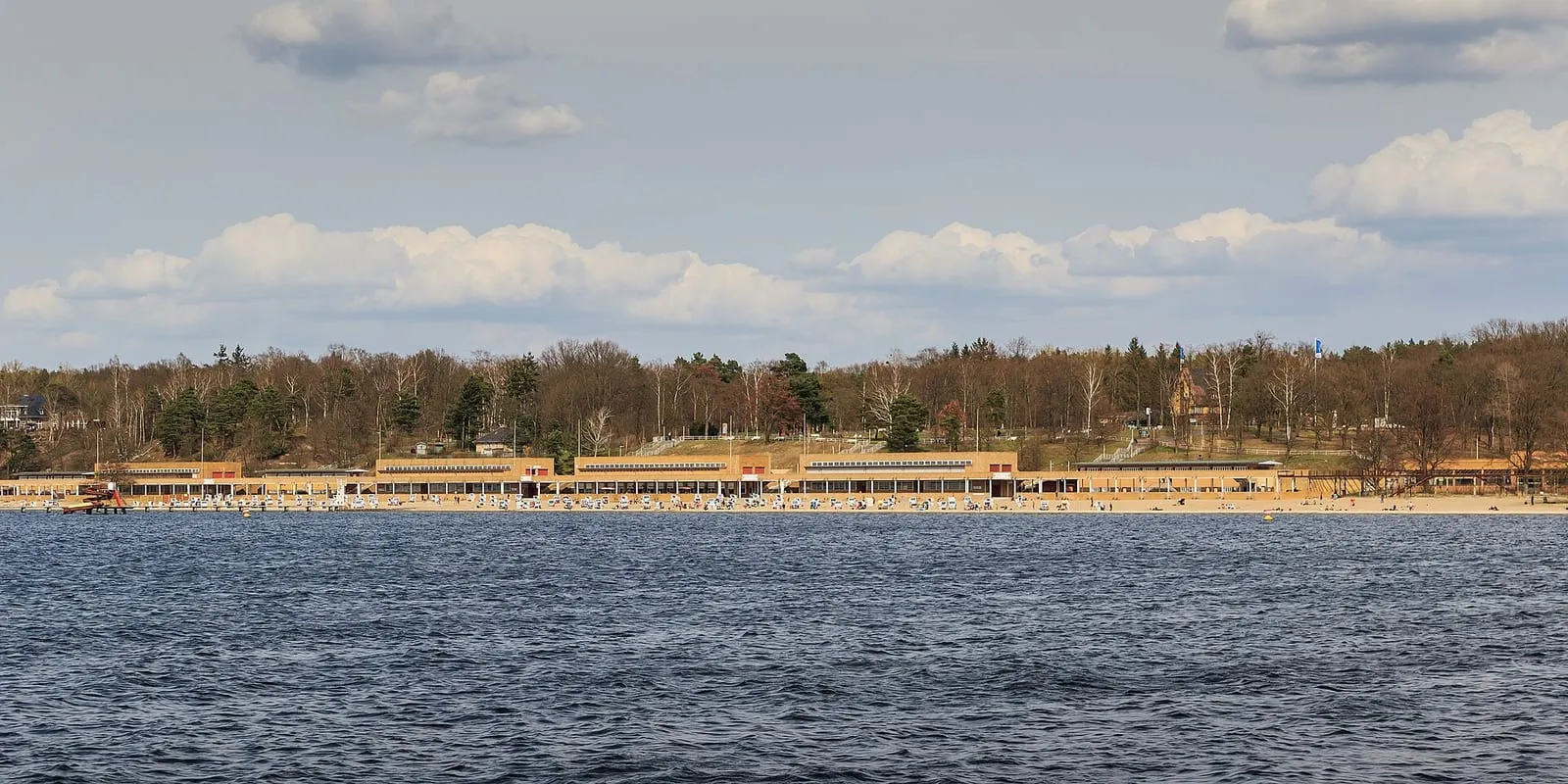 Le Strandbad Wannsee vu depuis le lac, sa longue plage de sable bordée de chaises longues devant les bâtiments historiques du lido