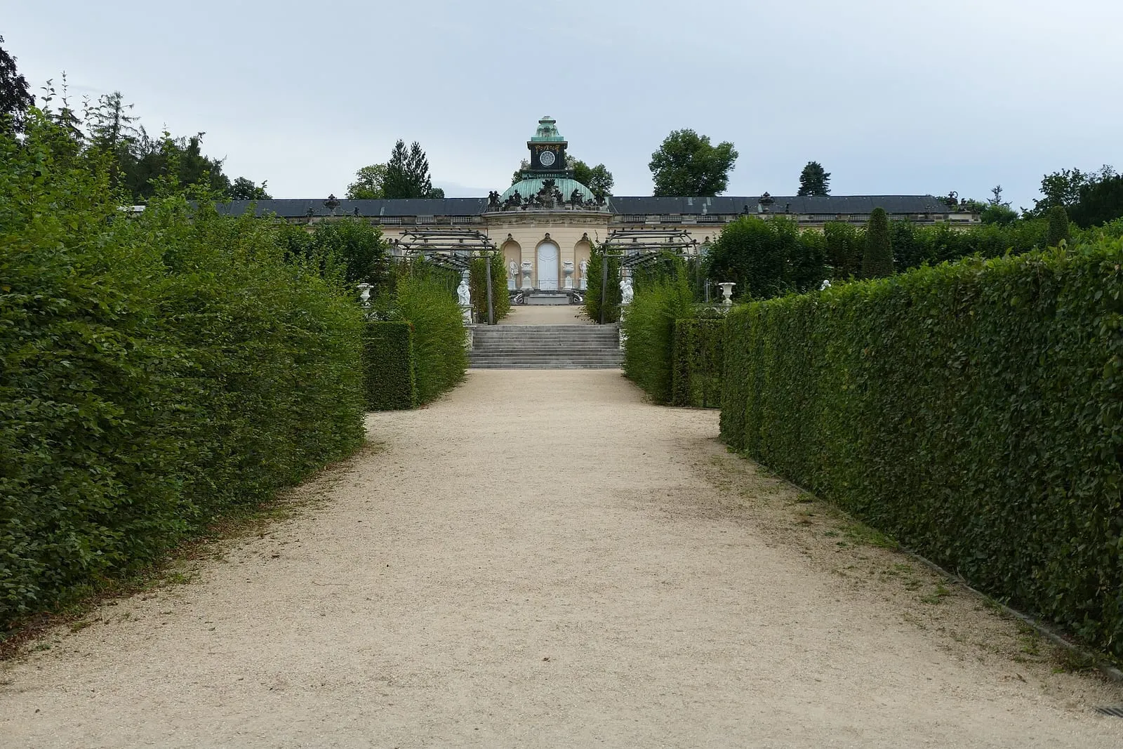 L'allée de gravier bordée de haies taillées qui mène à la galerie de peintures de Sanssouci et à son dôme vert surmonté d'une horloge