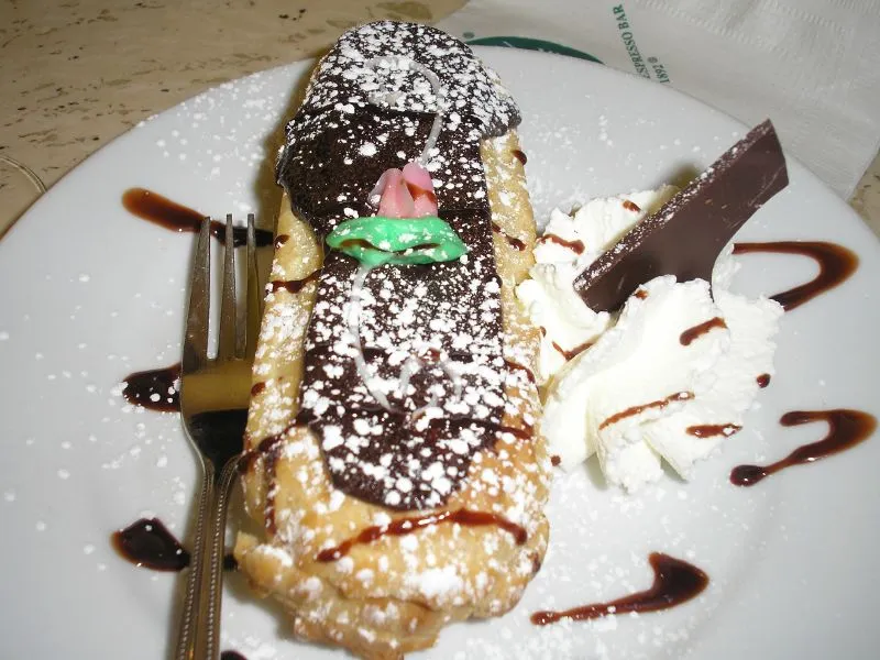 Un éclair au chocolat garni de chantilly et saupoudré de sucre glace, posé sur une assiette