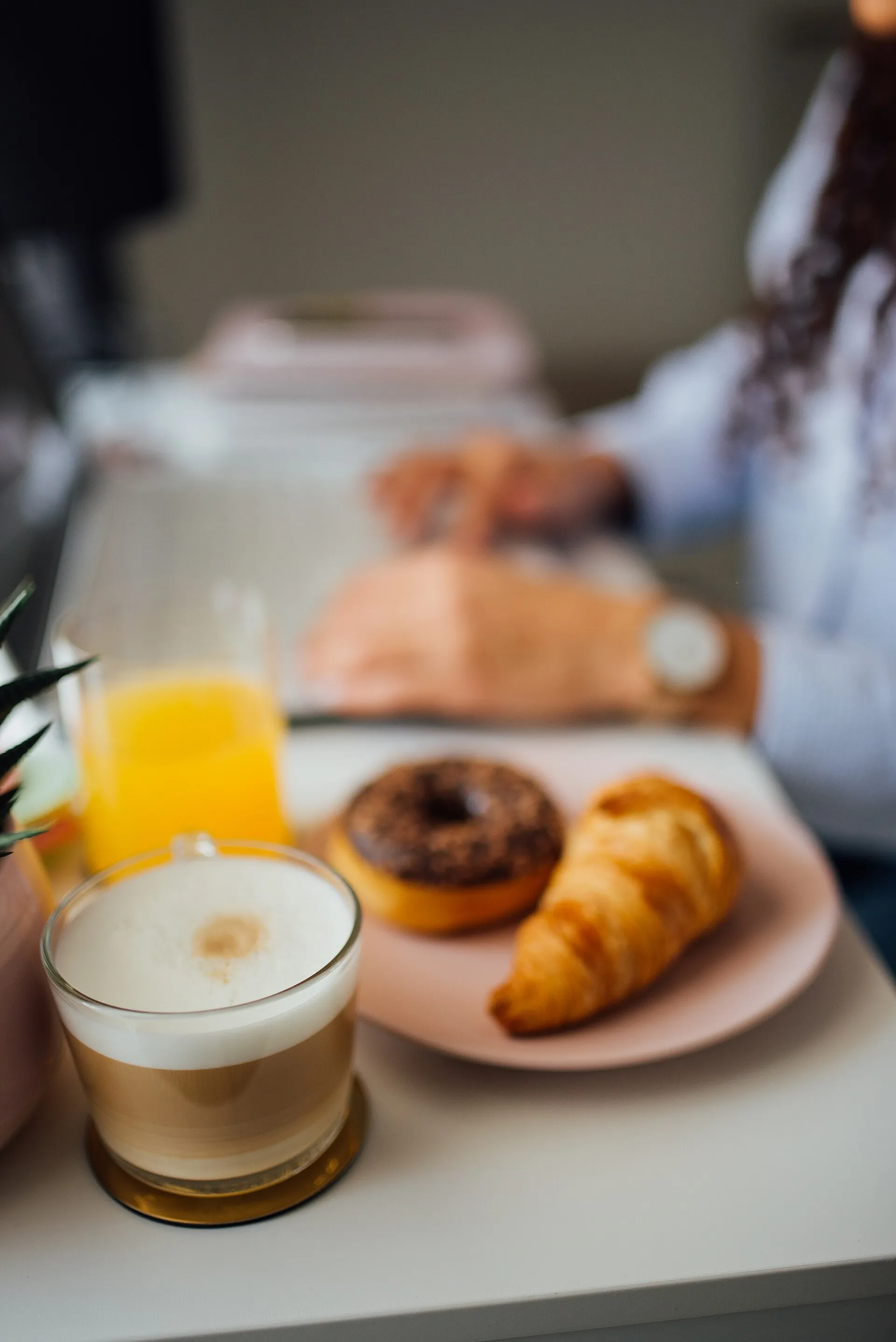 Petit déjeuner sur une table claire : latte mousseux, jus d'orange, croissant et donut au chocolat