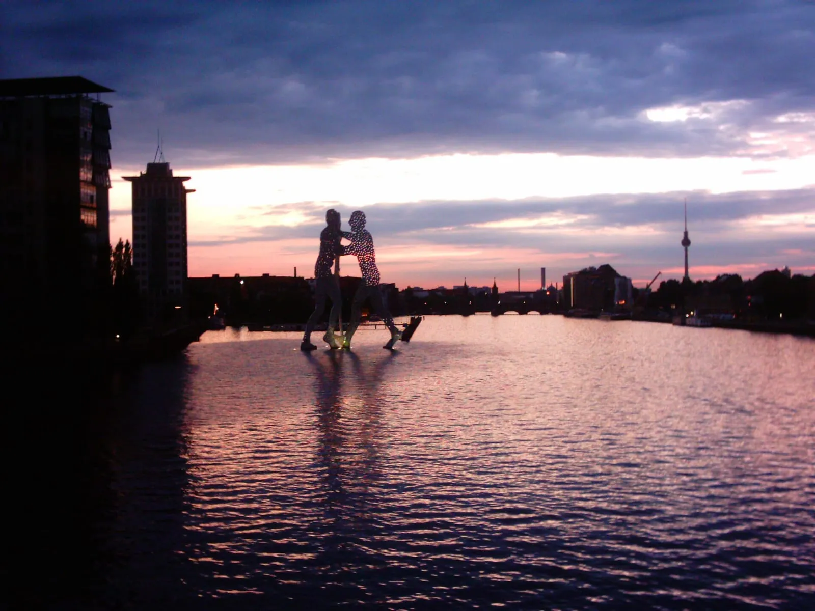 Le Molecule Man de Berlin vu depuis l'Elsenbrücke à l'heure bleue, trois silhouettes d'aluminium se détachant sur la Spree