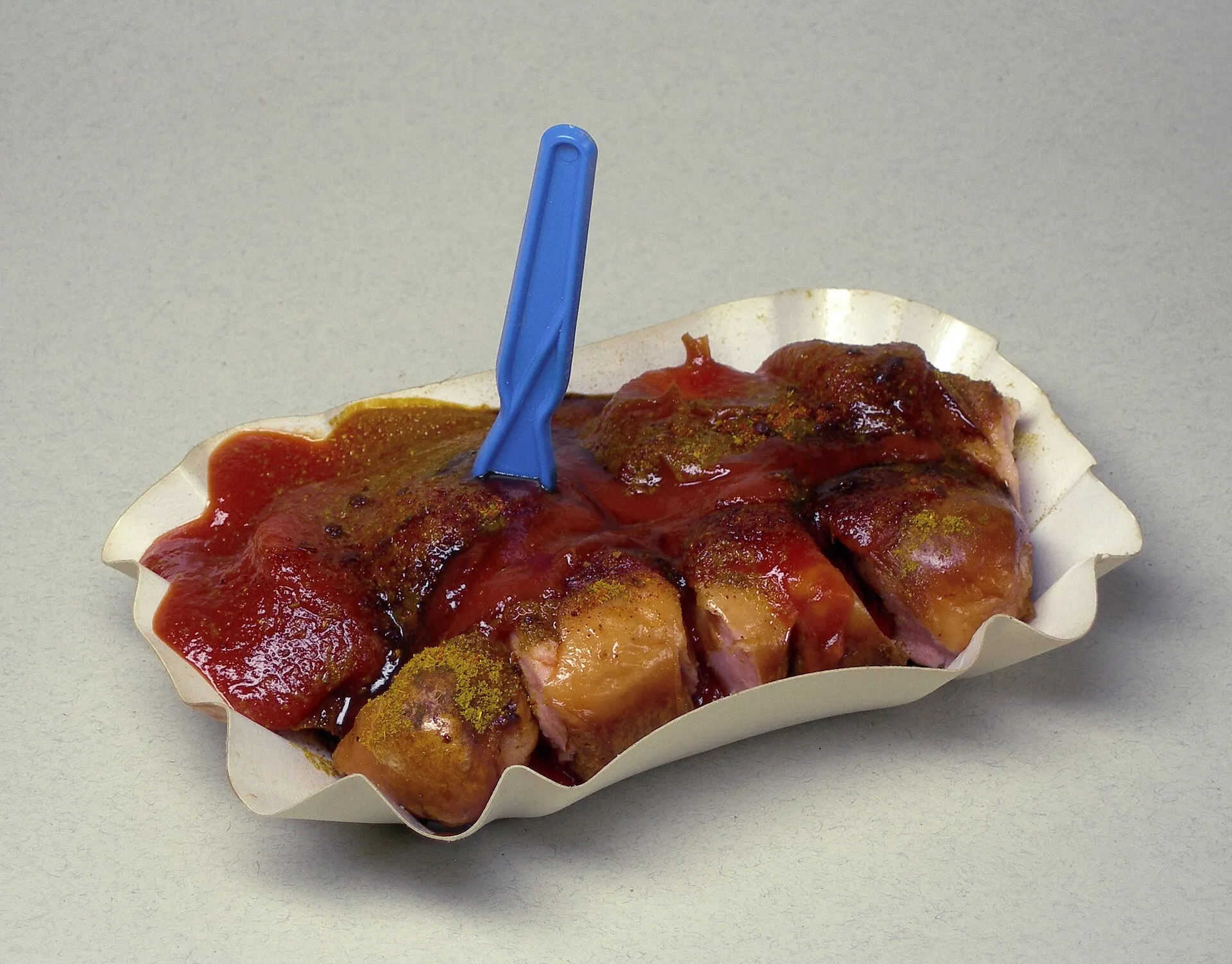 Une currywurst en barquette, nappée de sauce ketchup au curry et saupoudrée de poudre de curry