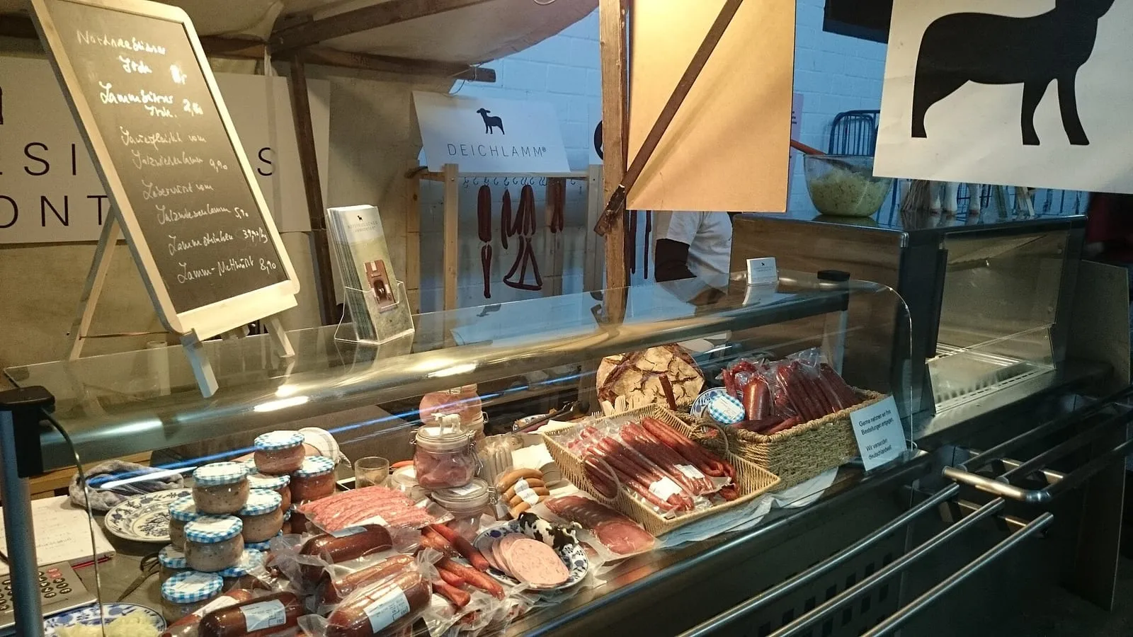 L’intérieur de la Markthalle Neun à Kreuzberg, avec un stand de charcuterie et sa carte de prix affichée