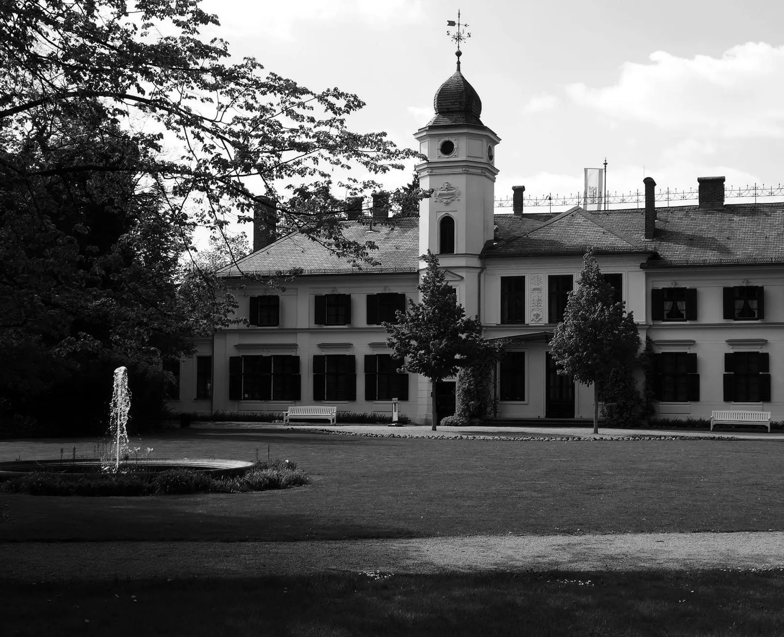 La façade du château de Britz et sa tour à bulbe, vues depuis la pelouse du parc avec un jet d'eau