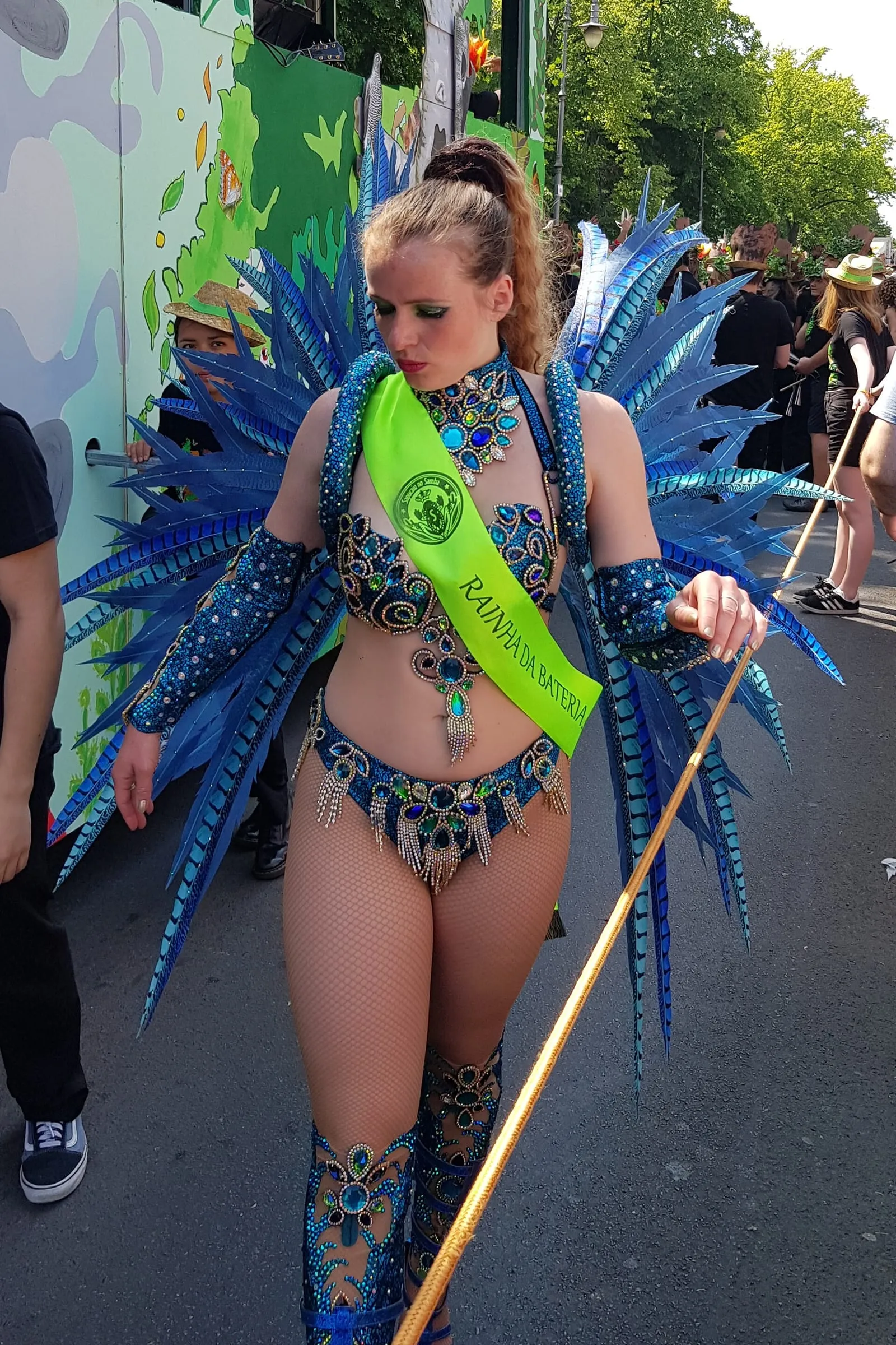 Participante au Carnaval des cultures de Berlin dans le défilé, costume bleu à plumes et écharpe verte au nom de l'événement