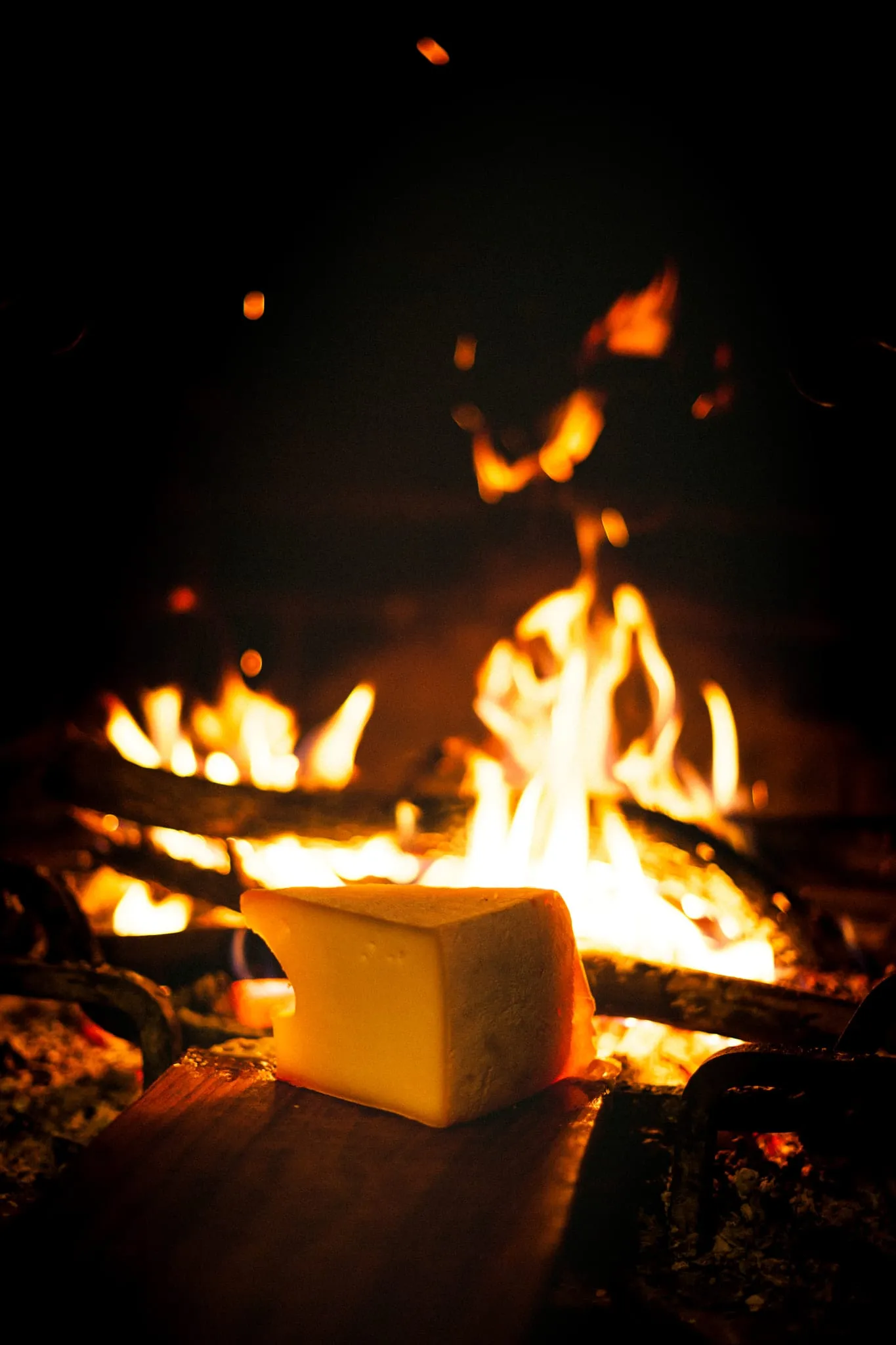 Fromage à raclette qui fond contre un feu de bois, servi avec des pommes de terre et de la charcuterie