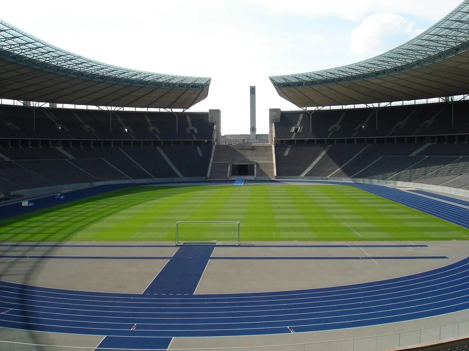 Intérieur du stade olympique de Berlin : tribunes couvertes, pelouse et piste d'athlétisme bleue