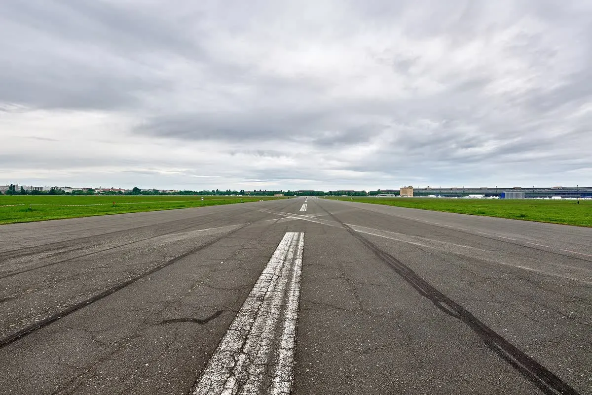 L'ancienne piste d'atterrissage du Tempelhofer Feld, longue bande d'asphalte marquée de blanc et bordée de pelouses, la ville à l'horizon