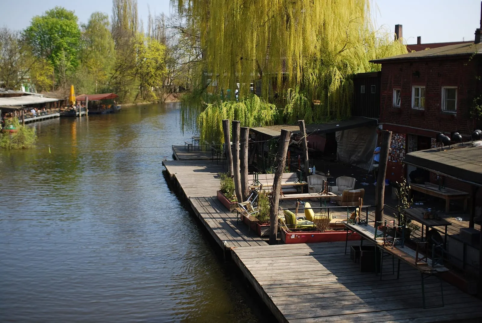 La terrasse en bois du Club der Visionäre sur le Flutgraben, sous un saule pleureur, avec le canal à gauche