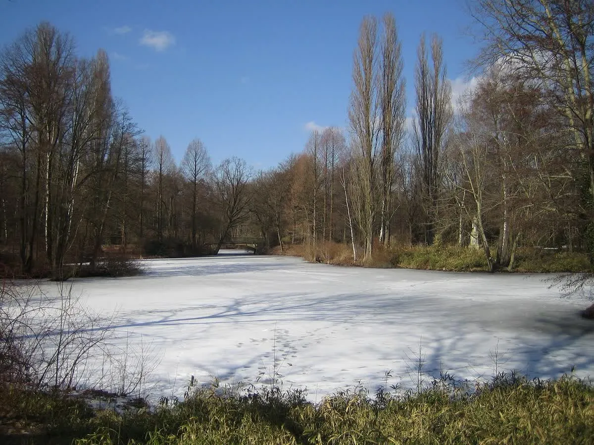 Un étang gelé du Tiergarten en hiver, entouré de peupliers dénudés et d'un petit pont de pierre